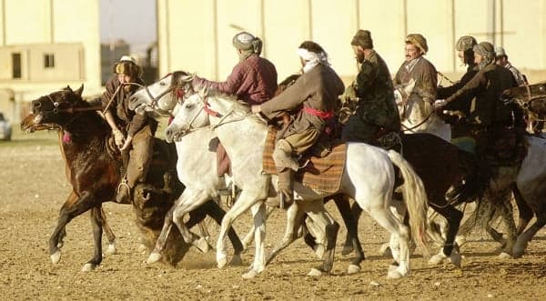 A group of riders in traditional dress galloping on horseback during a buzkashi match