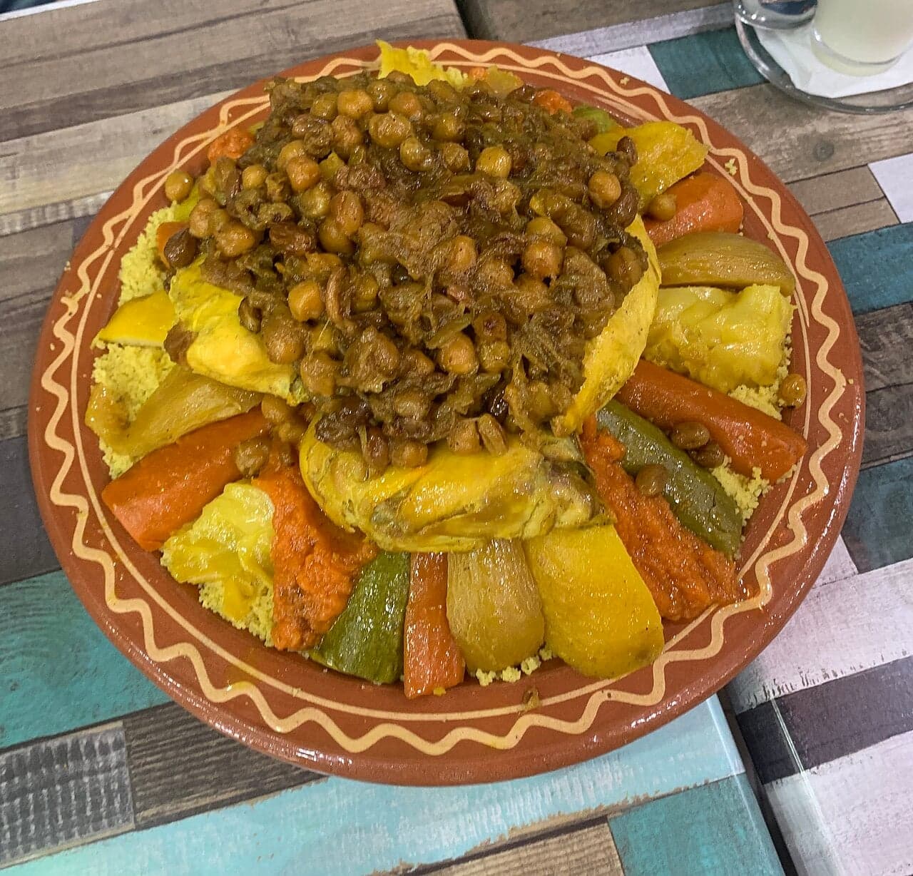 A round platter of fluffy yellow couscous topped with carrots, courgettes, chickpeas and lamb