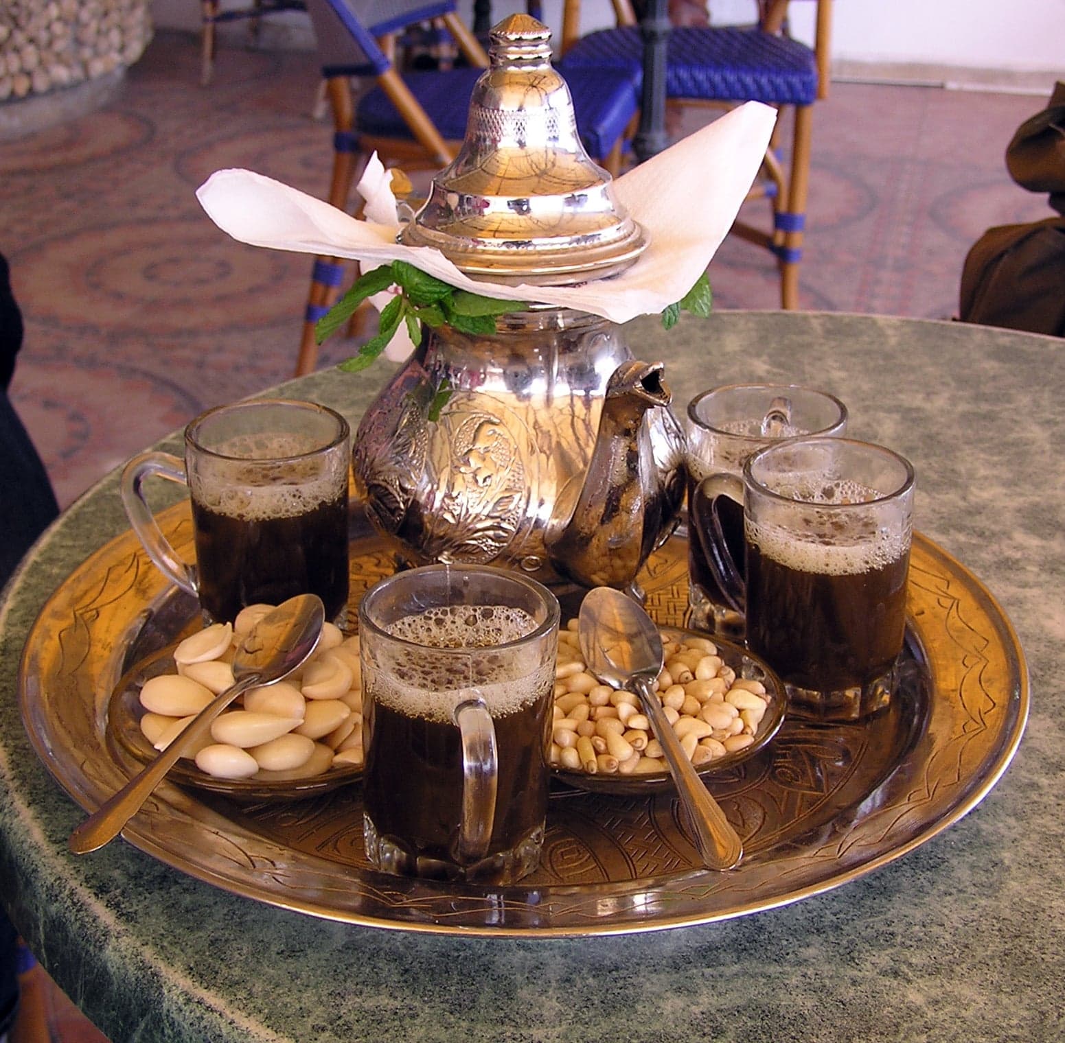 Hot Algerian mint tea being poured from a silver teapot into small decorated glasses