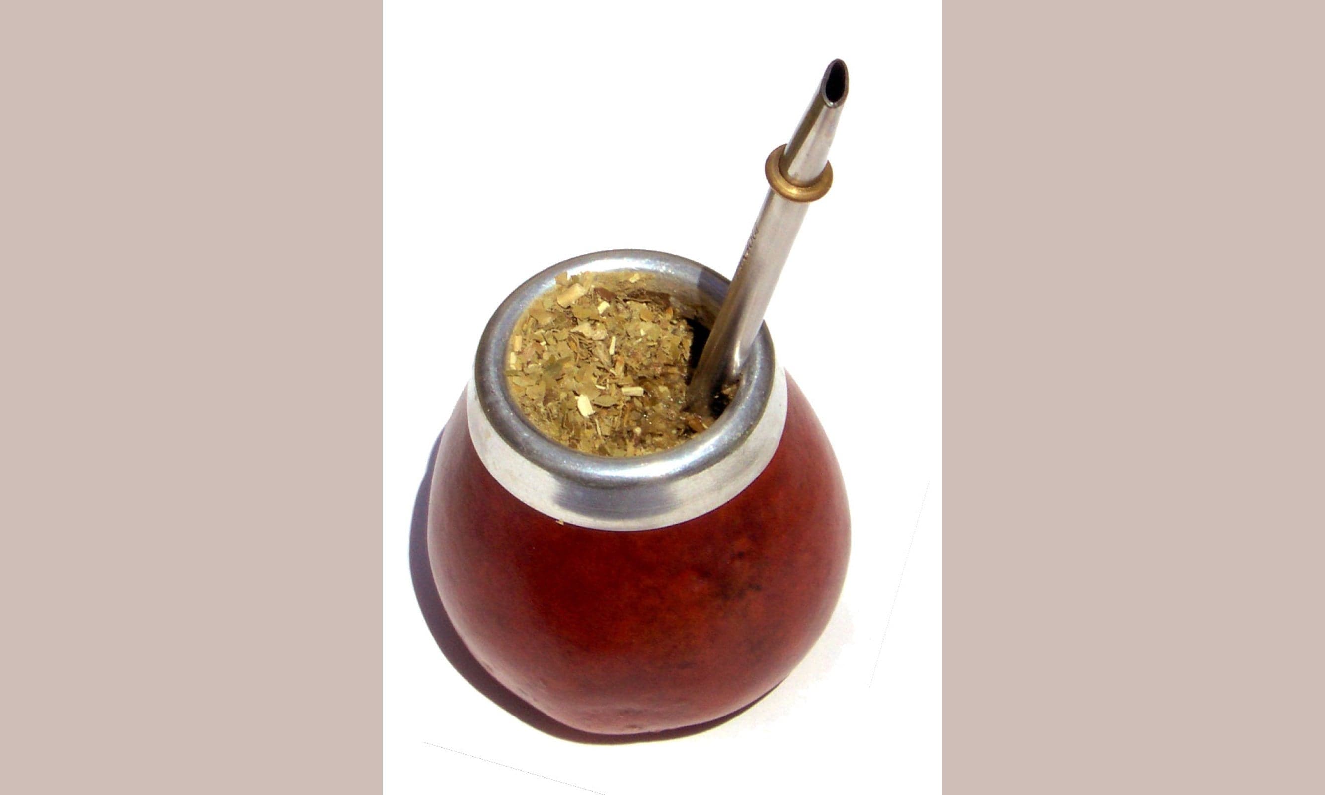 A traditional mate gourd cup with a metal straw and green leaves inside