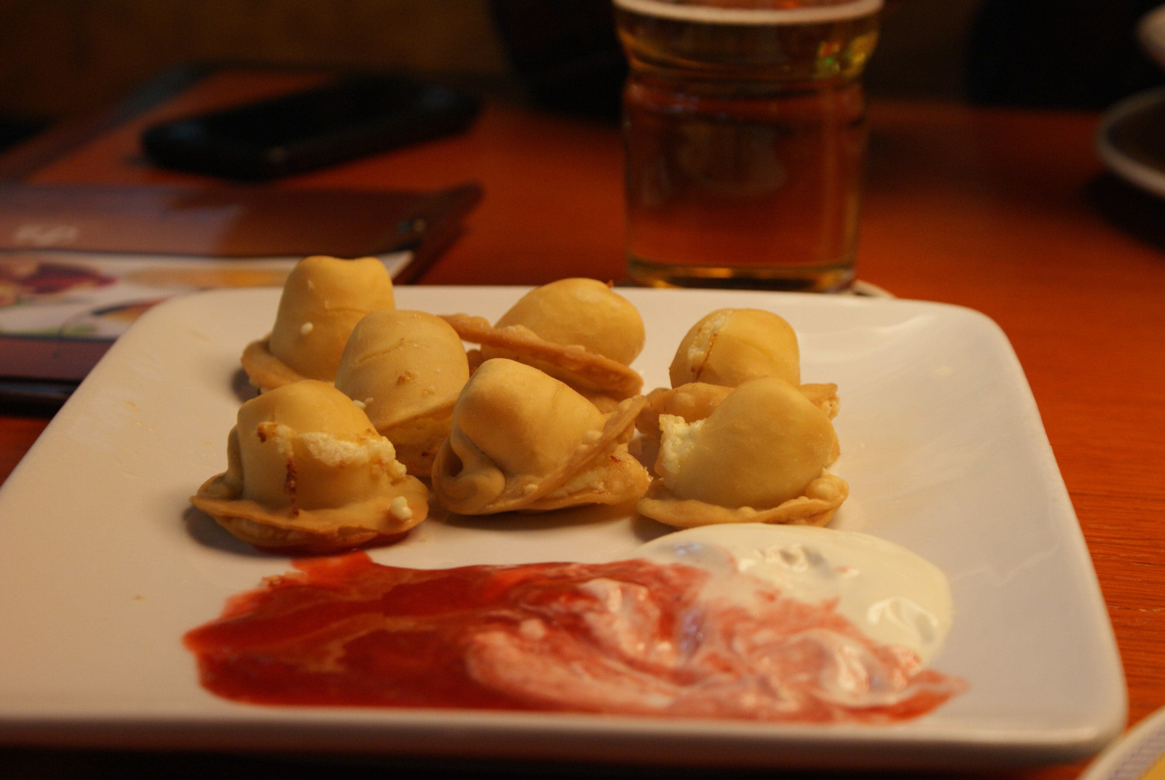 A bowl of steaming kalduny dumplings garnished with fried onion and butter