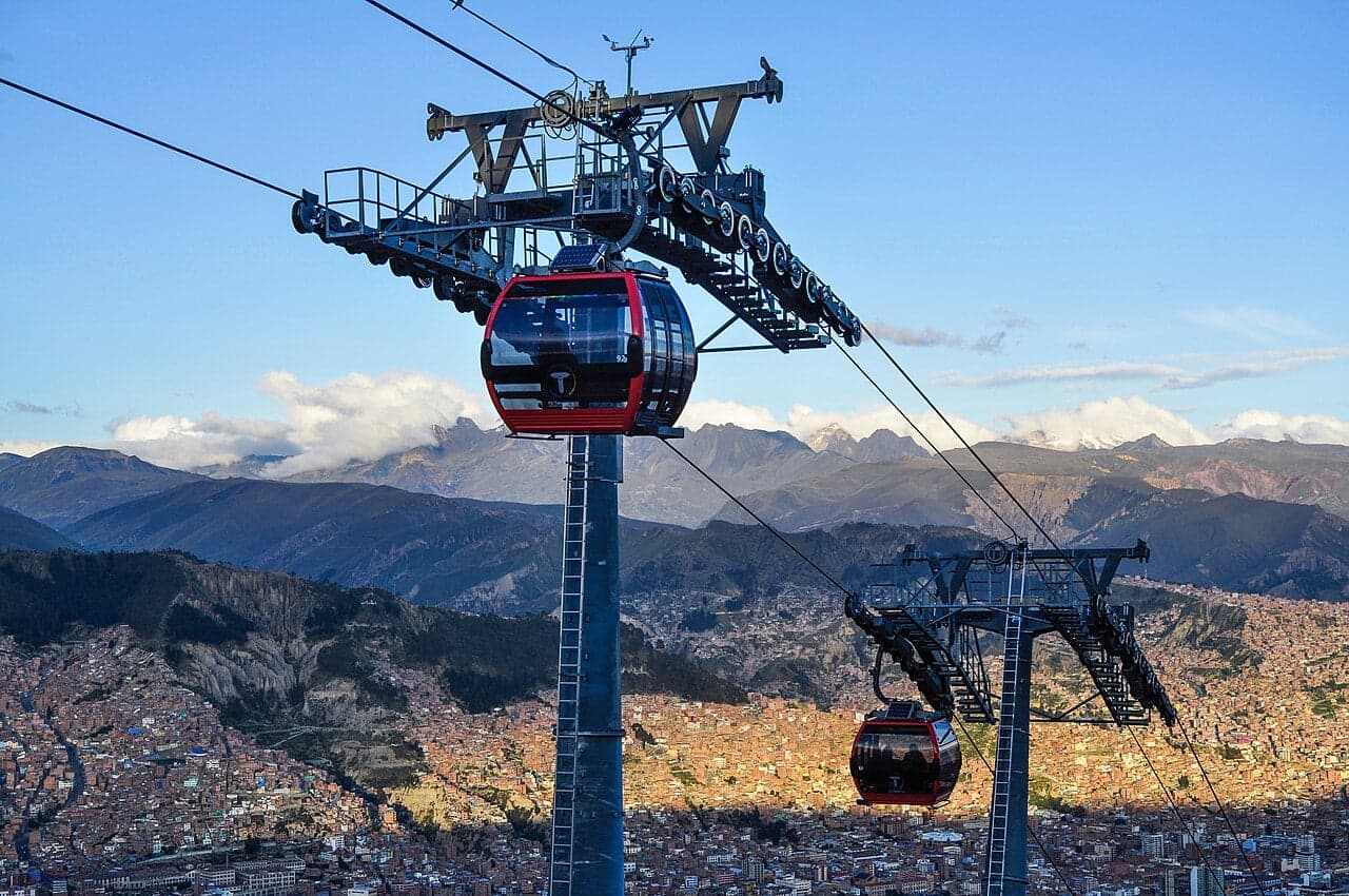 Red cable cars gliding over the rooftops of La Paz with snowy Mount Illimani in the background