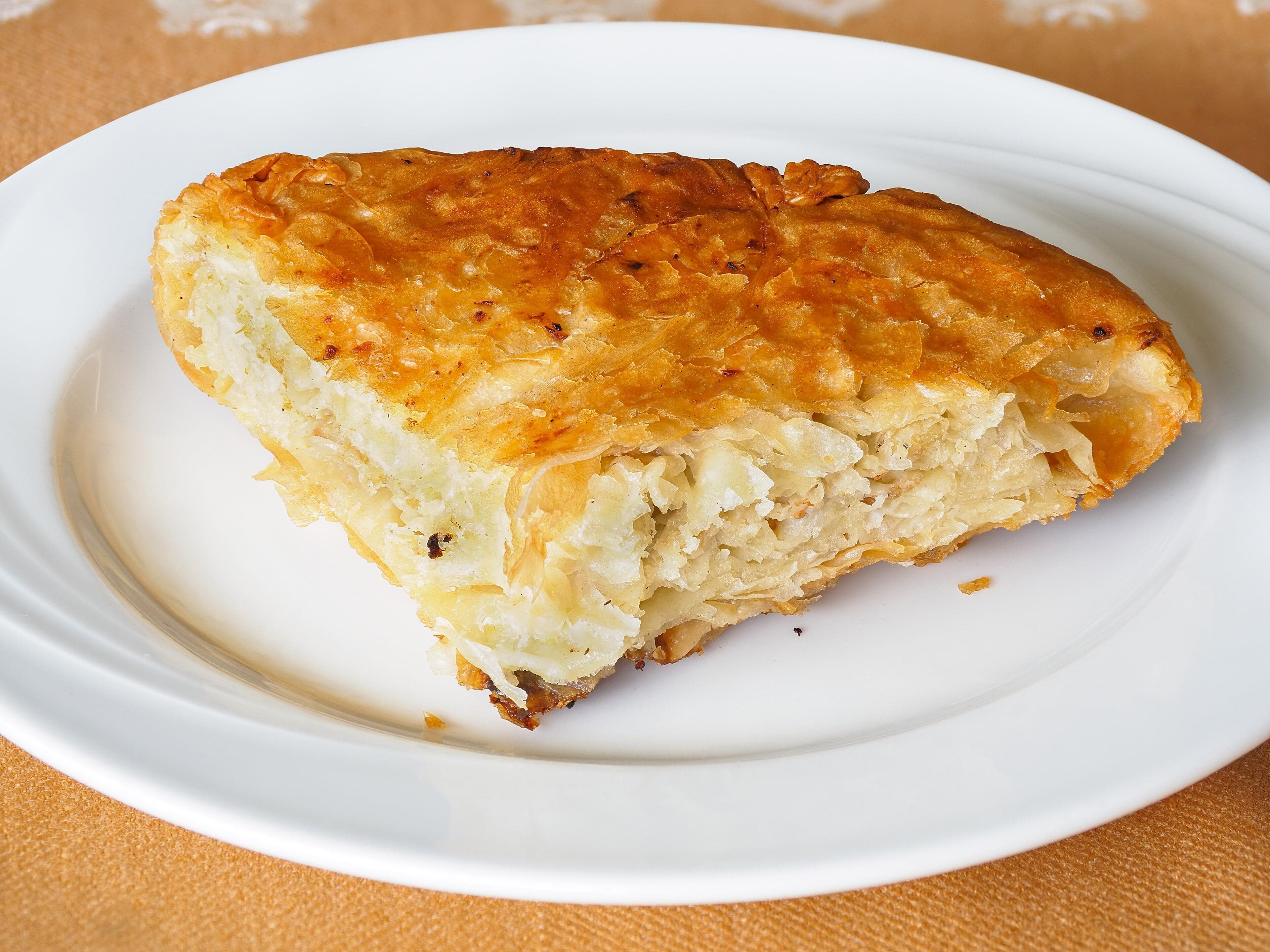A golden spiral of Bosnian burek pastry glistening with oil on a round tray