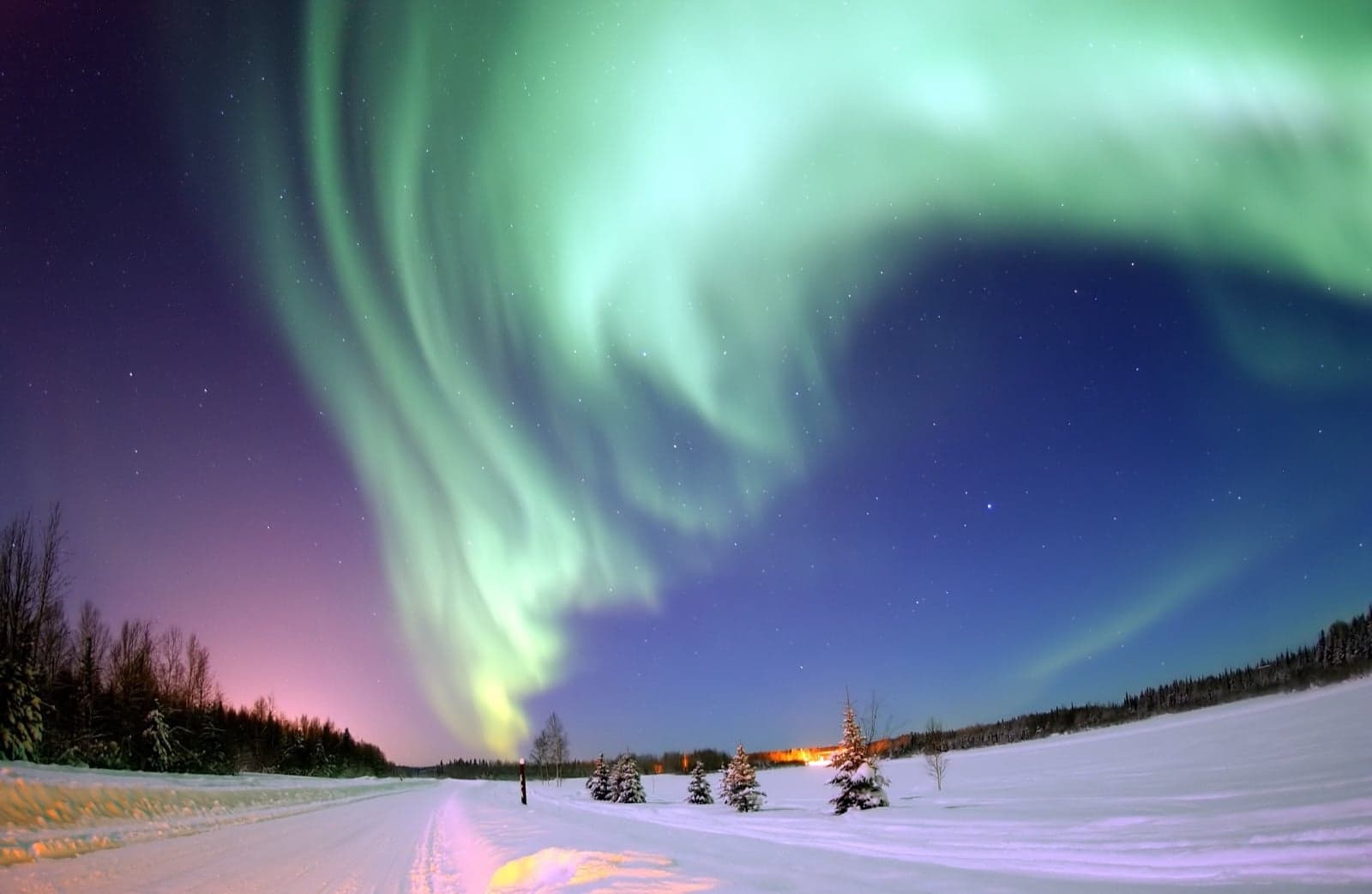 Green ribbons of the Northern Lights swirling above a snowy landscape