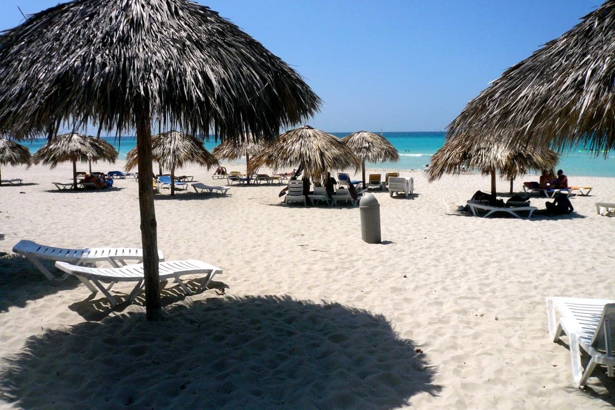 A long empty white-sand beach with turquoise sea and green palm trees in Cuba