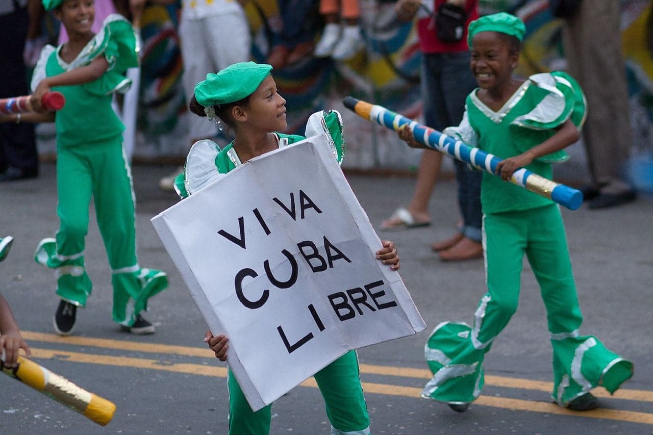 Costumed dancers in bright feathered outfits parading through Santiago de Cuba at night