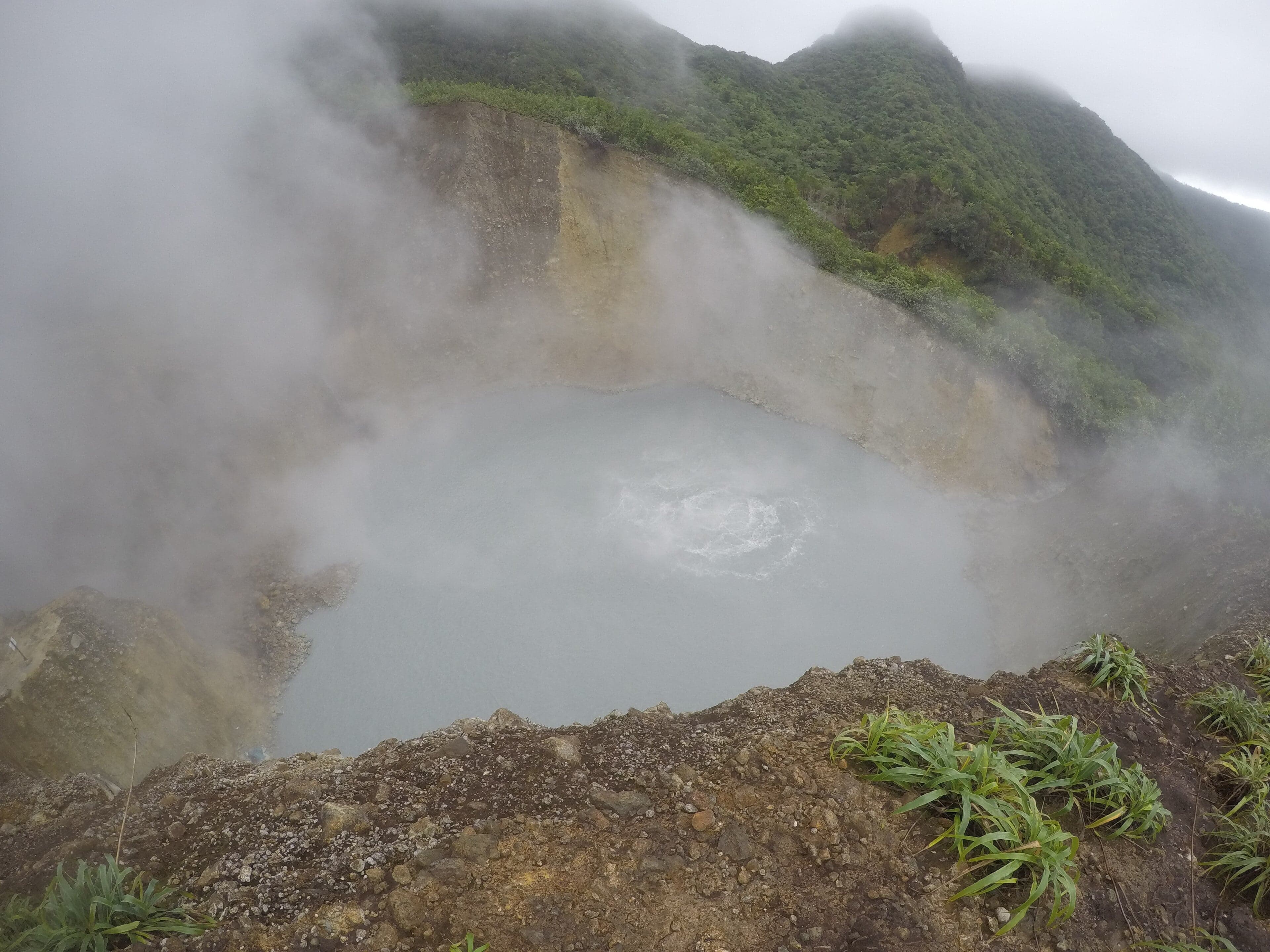 Boiling Lake in Dominica surrounded by misty grey cliffs and steam rising from the water