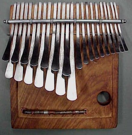 A wooden likembe thumb piano with metal tines held in a pair of hands