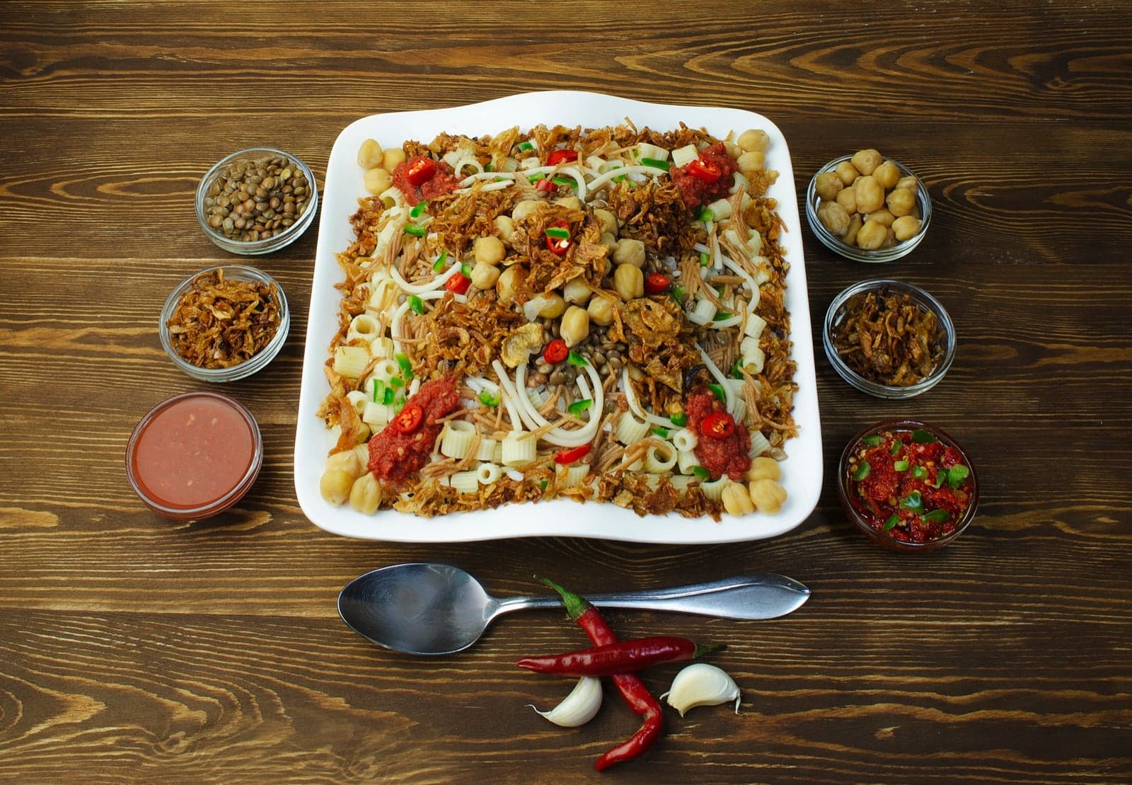 A plate of koshari with crispy onions, sauces and side dishes