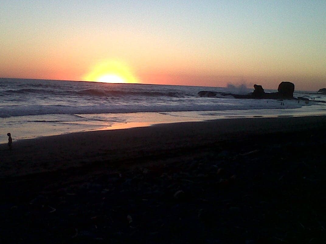 Surfers riding waves at El Tunco beach with dark volcanic sand