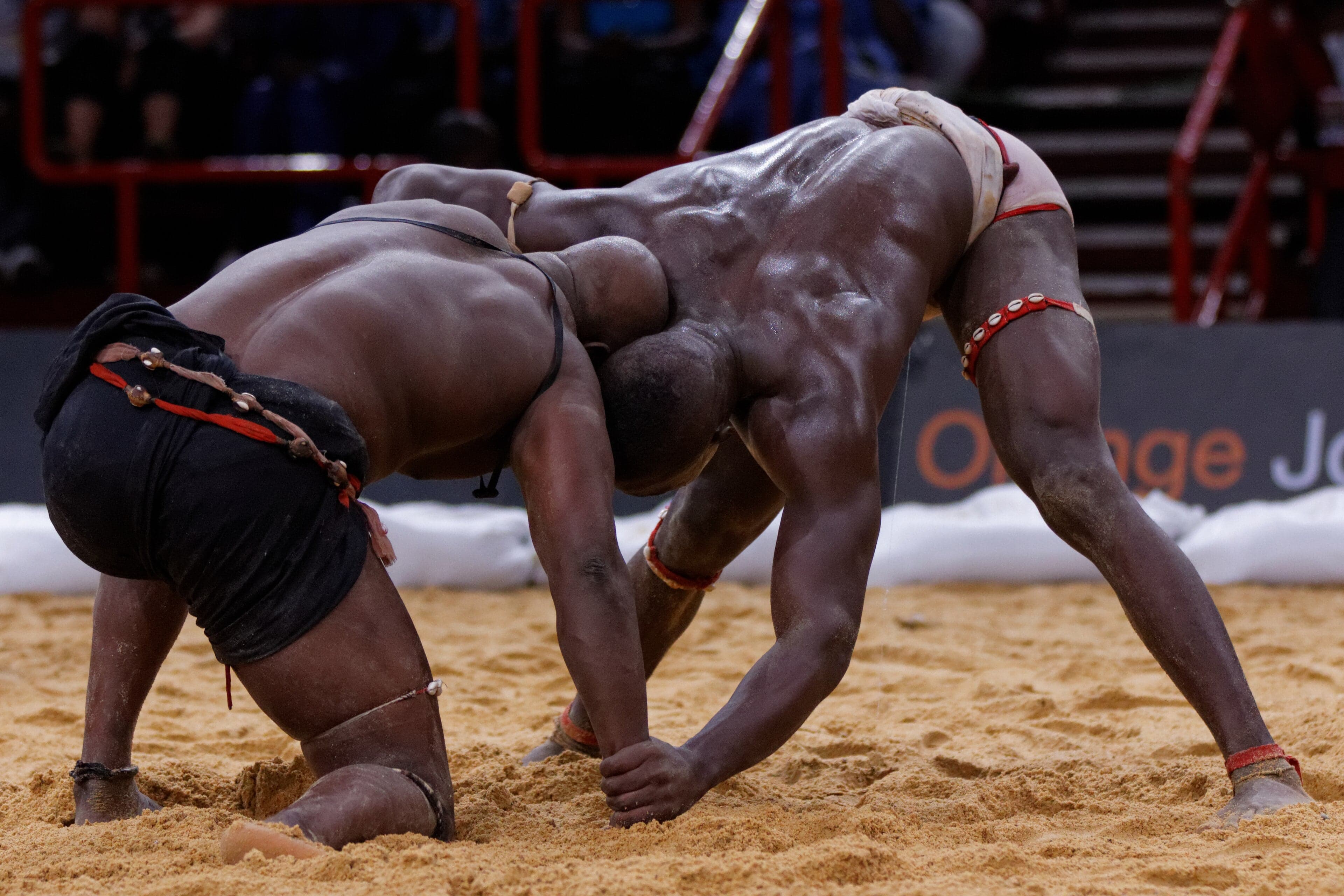 Two wrestlers competing in a sandy arena surrounded by cheering spectators