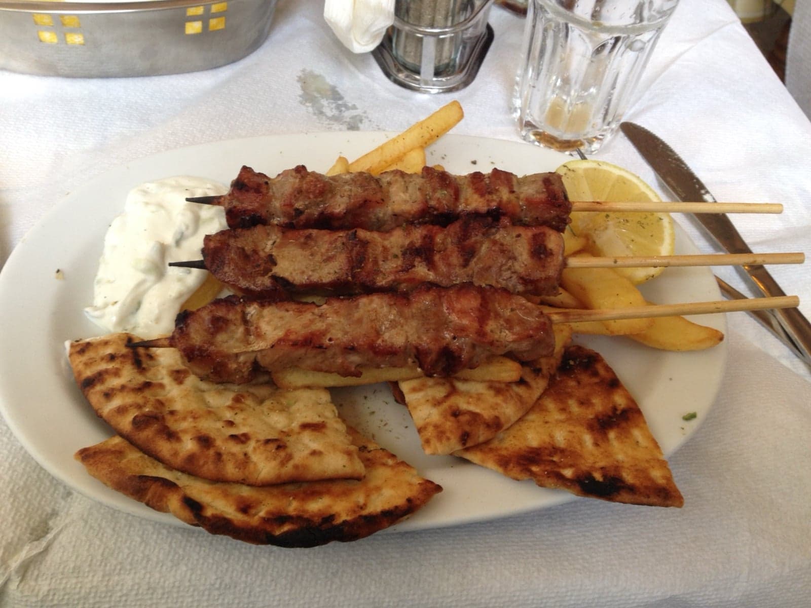 Souvlaki skewers grilling over charcoal with pita bread alongside