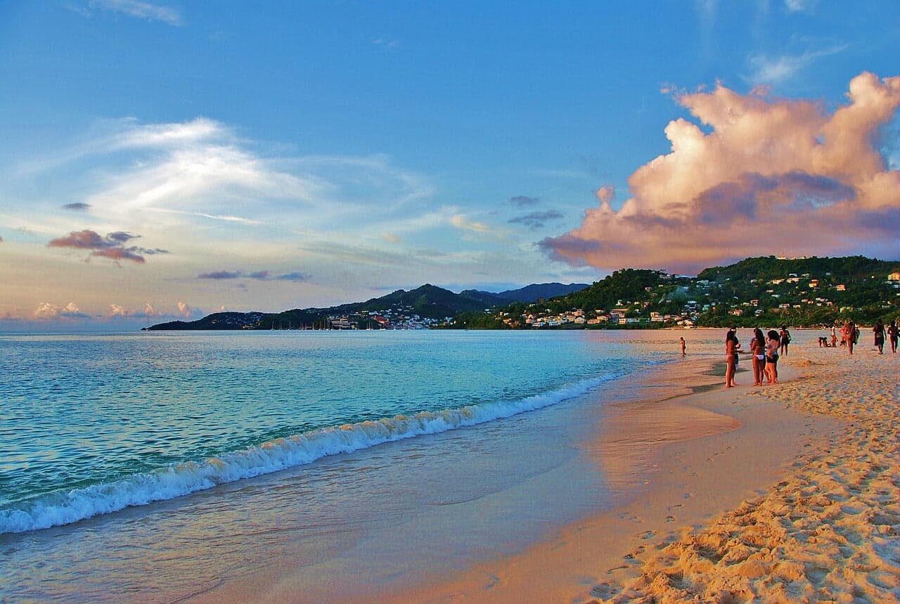 A wide arc of white sand at Grand Anse Beach with calm turquoise water and green hills behind