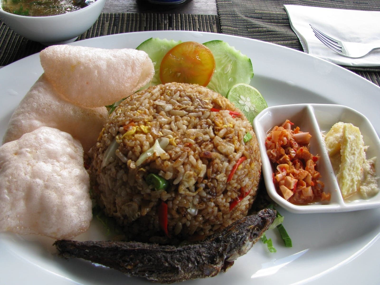 A plate of golden-brown nasi goreng with prawn crackers, cucumber and tomato