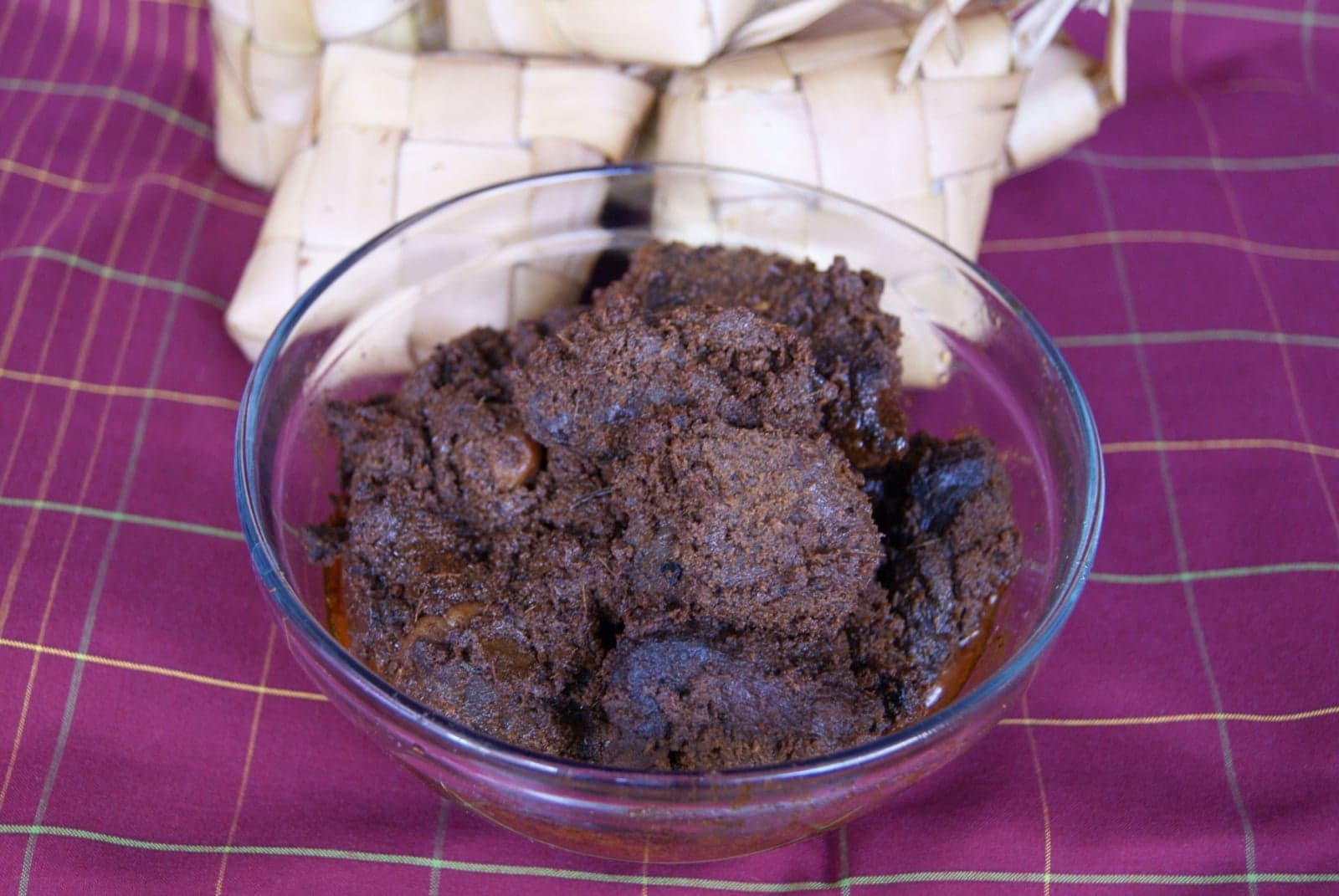A bowl of dark-brown rendang beef next to woven rice parcels