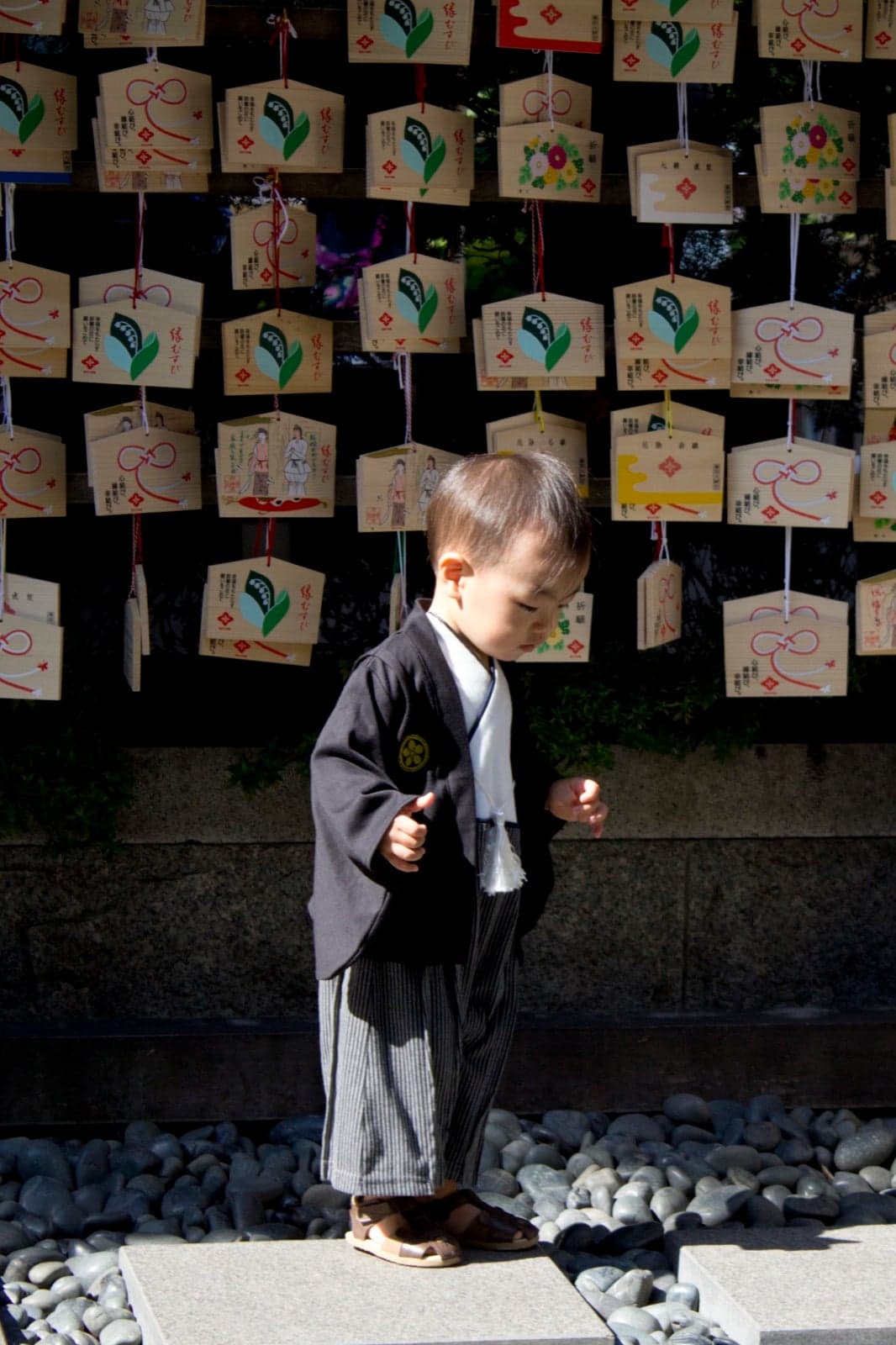 A young boy in traditional Japanese clothes standing in front of wooden ema prayer plaques