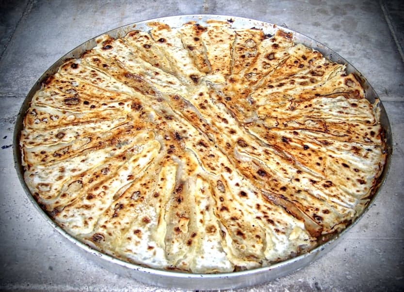 A round flia layered pancake being cooked over an open fire with cream between the layers