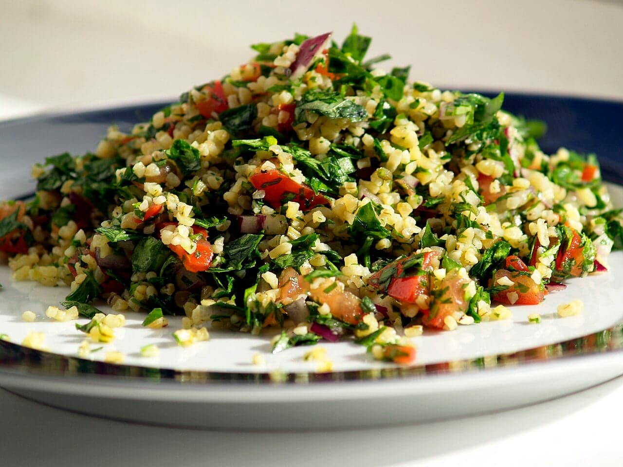 A bright green bowl of tabbouleh with chopped parsley, tomato and bulgur
