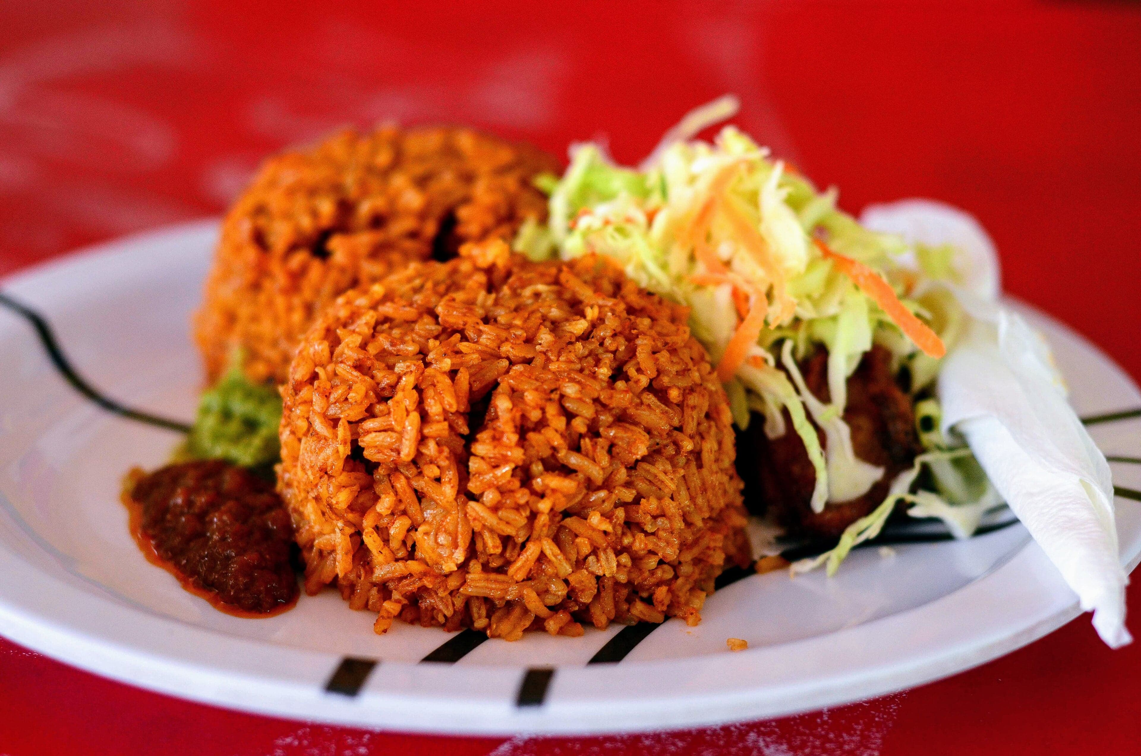 A large pot of Liberian jollof rice, bright orange-red, garnished with sliced onions and green herbs
