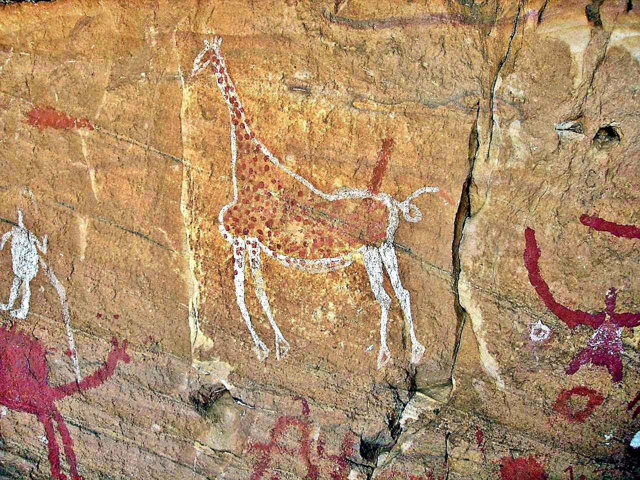 Red and orange prehistoric animal paintings on a sandstone rock face in the Sahara