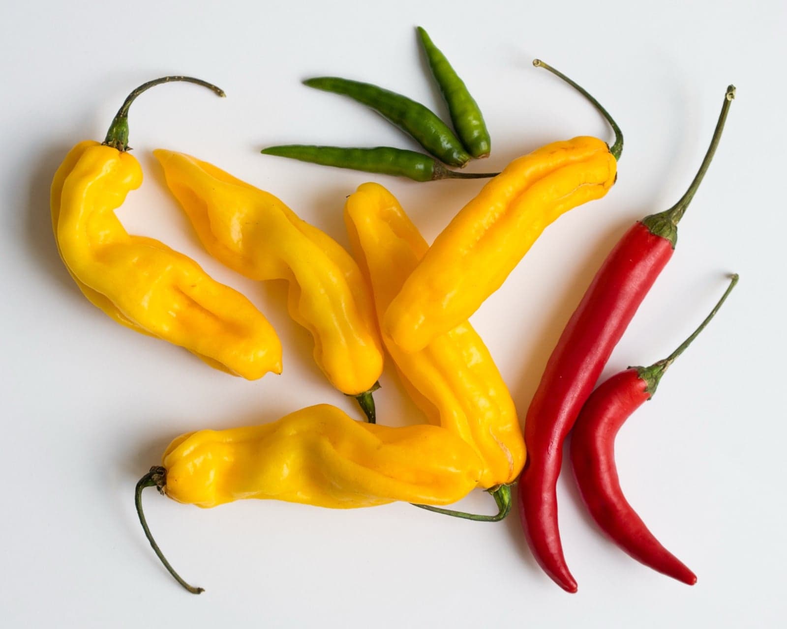 Yellow, red and green chillies arranged on a white surface