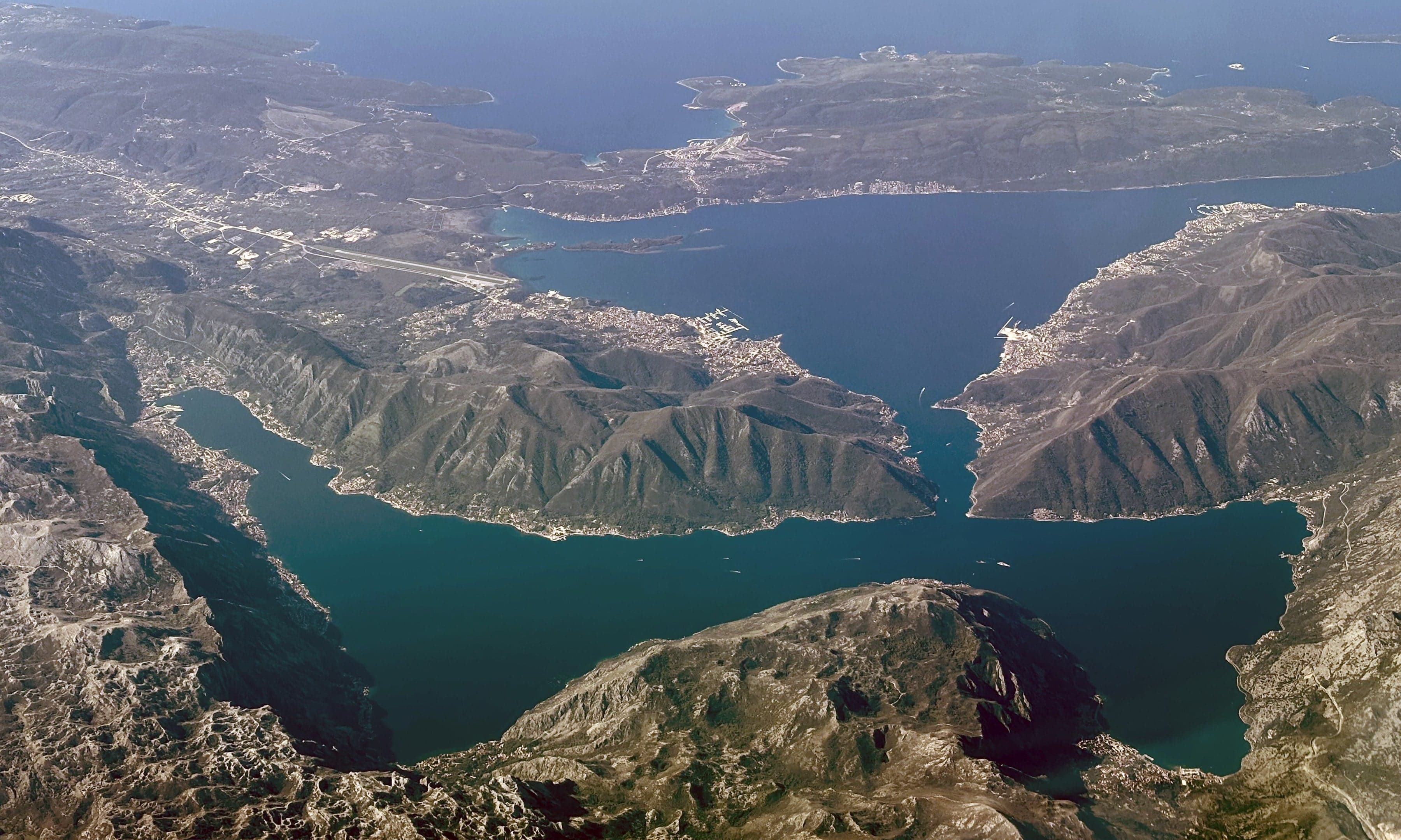 The calm blue waters of the Bay of Kotor with old stone town walls and mountains rising behind