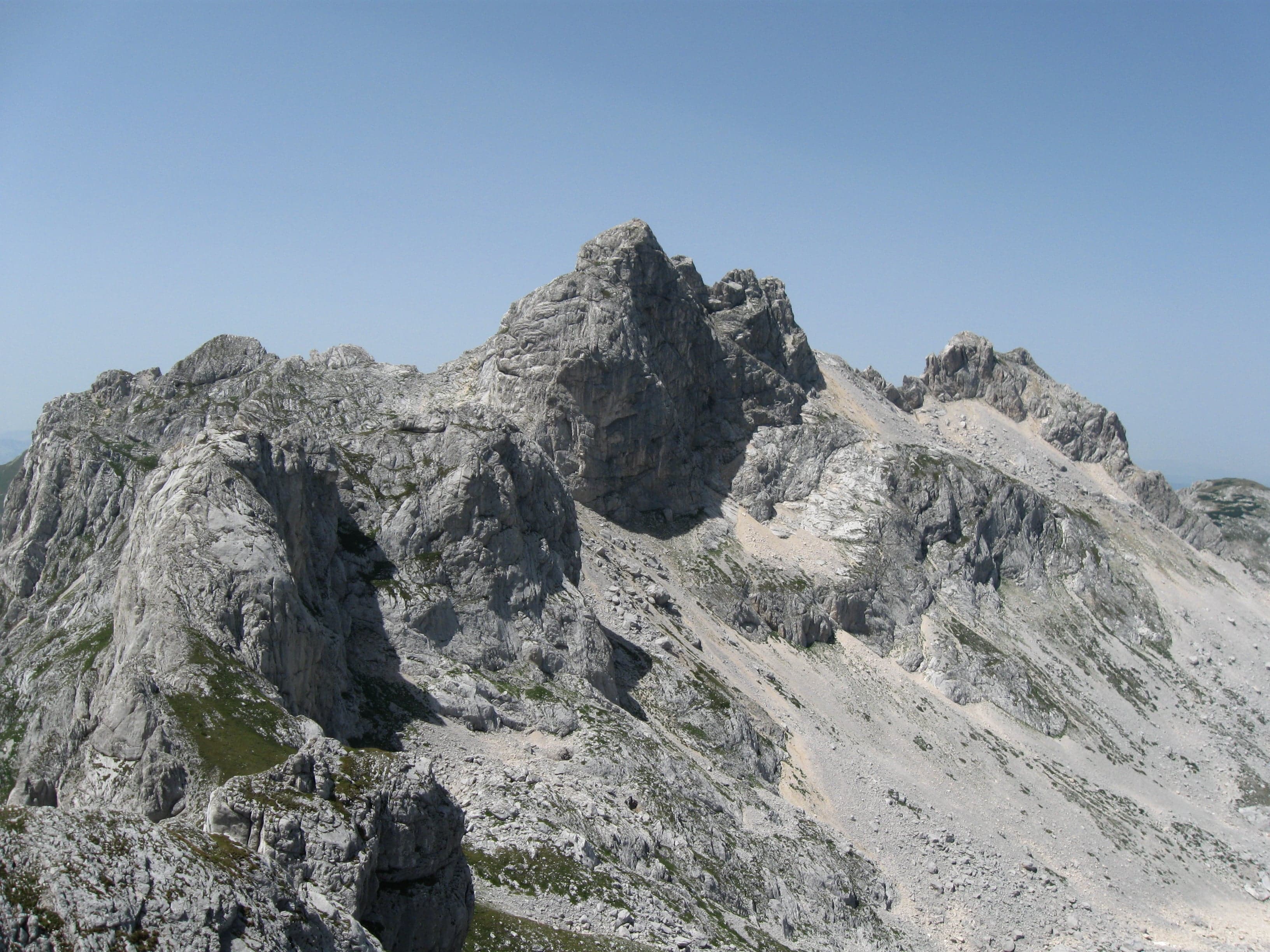 The rocky summit of Bobotov Kuk rising above snow fields with a wide blue sky behind