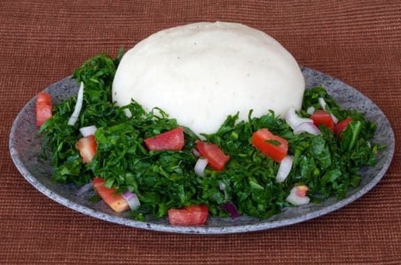 A mound of smooth white xima maize porridge on a plate with a vegetable stew alongside