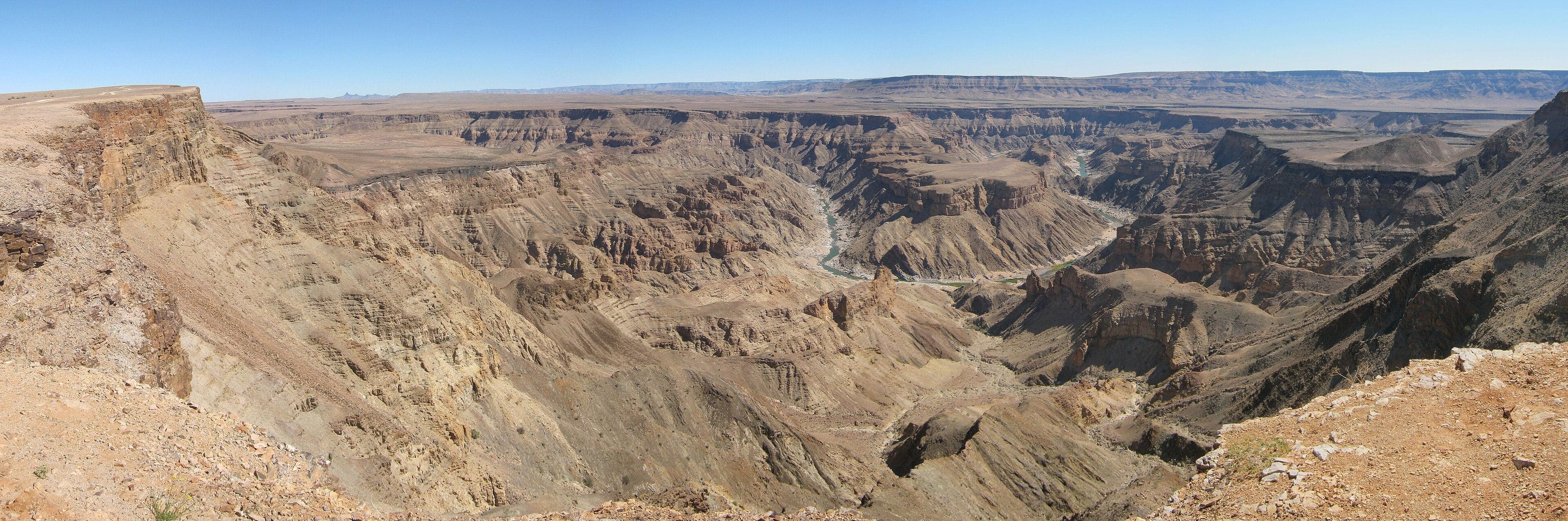A vast rocky canyon stretching to the horizon under a wide blue sky