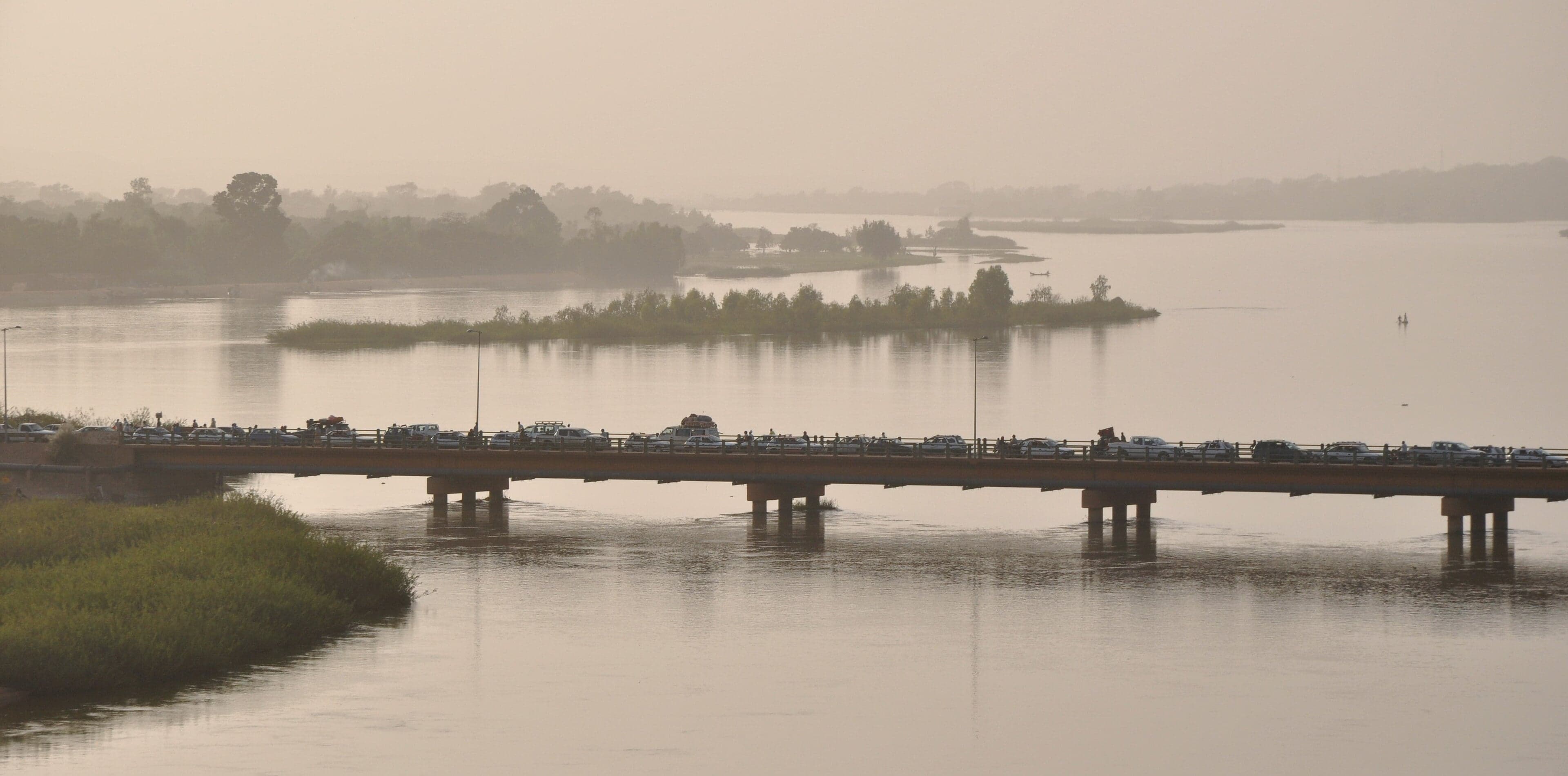 The wide Niger River with boats and green banks at sunset