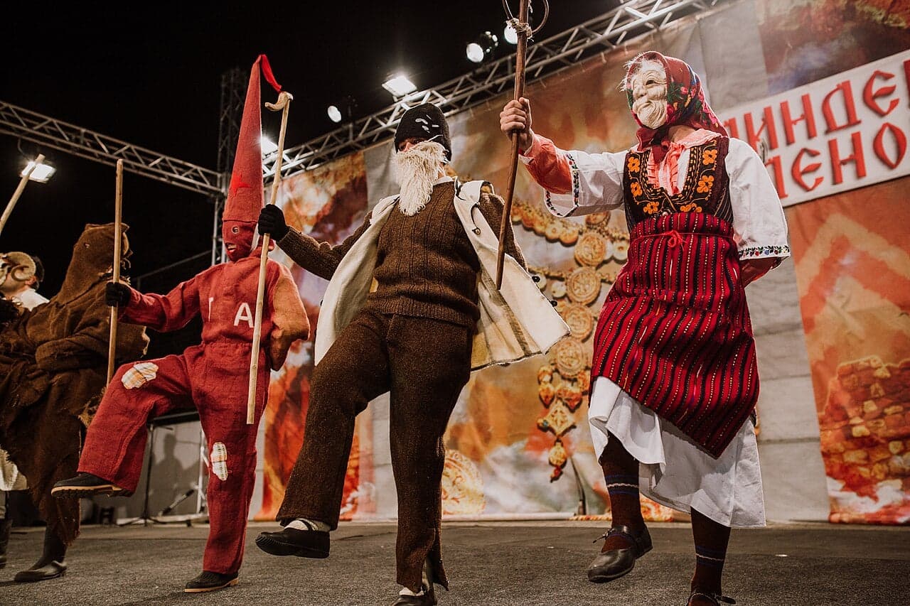 People in wild handmade masks and colourful costumes parading through a snowy village street