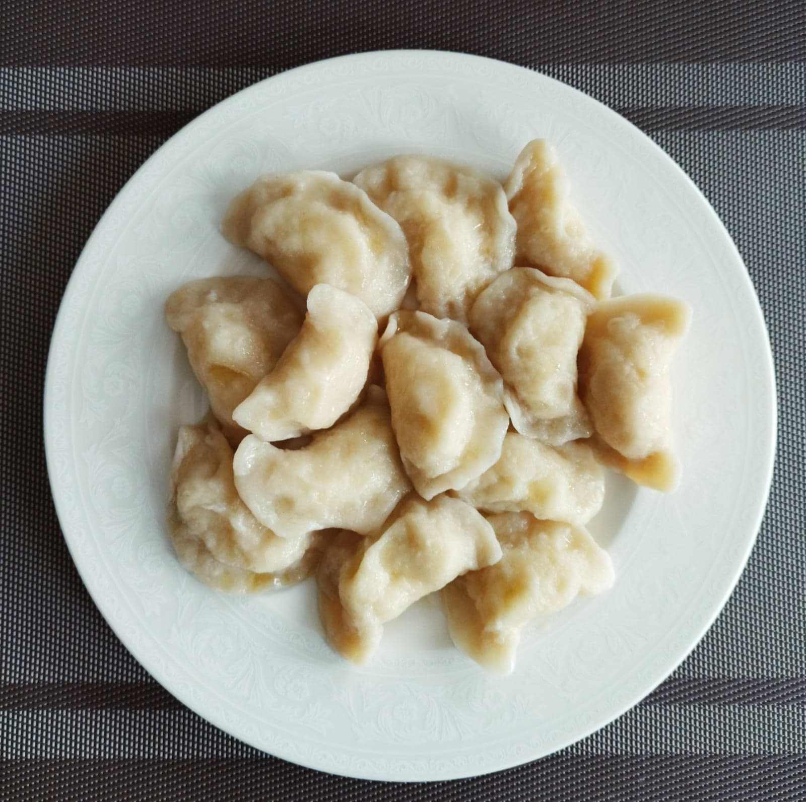 A plate of golden Polish pierogi with sour cream and herbs
