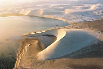 Golden sand dunes rising steeply from the calm turquoise water of Khor Al Adaid