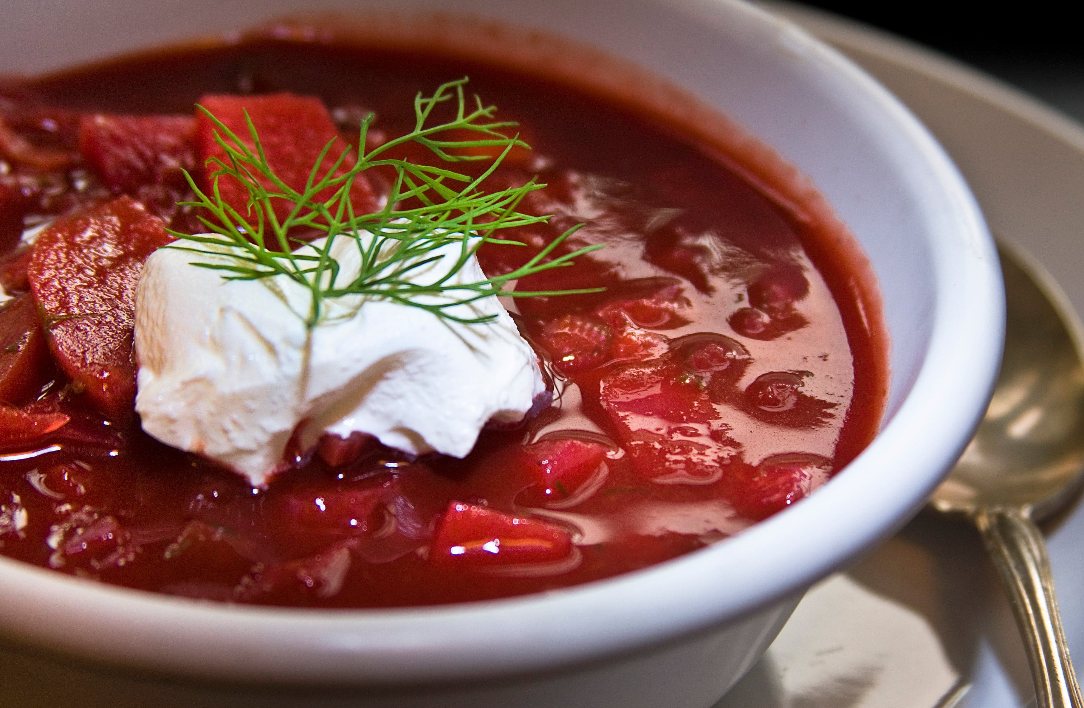 A bowl of deep red borscht topped with a spoonful of white sour cream and fresh dill