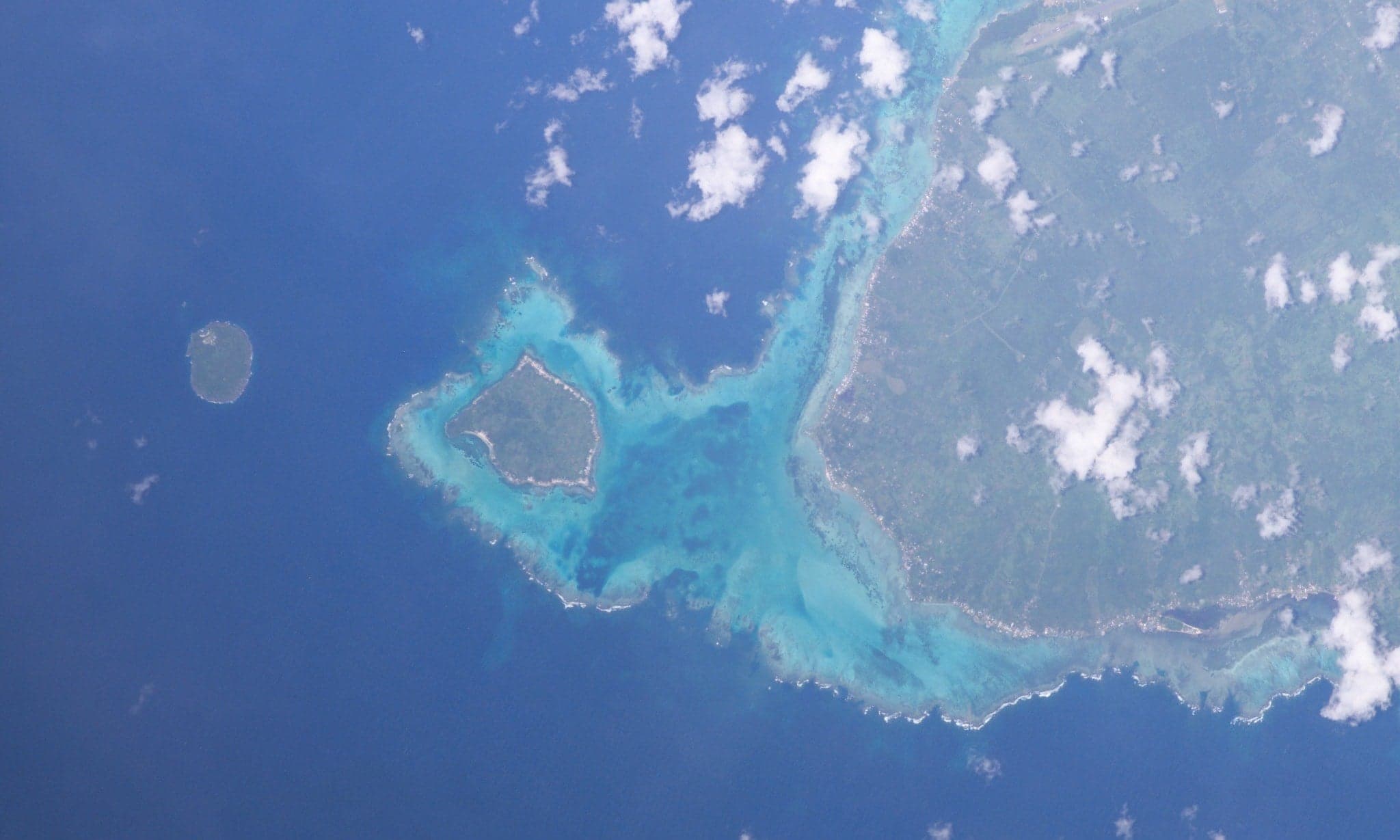 A small green island viewed from the water with clear blue sea in the foreground