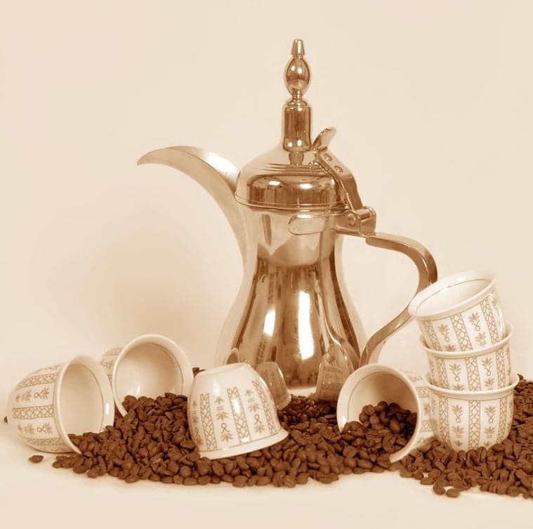 A traditional dallah coffee pot pouring pale gold Arabic coffee into a small cup
