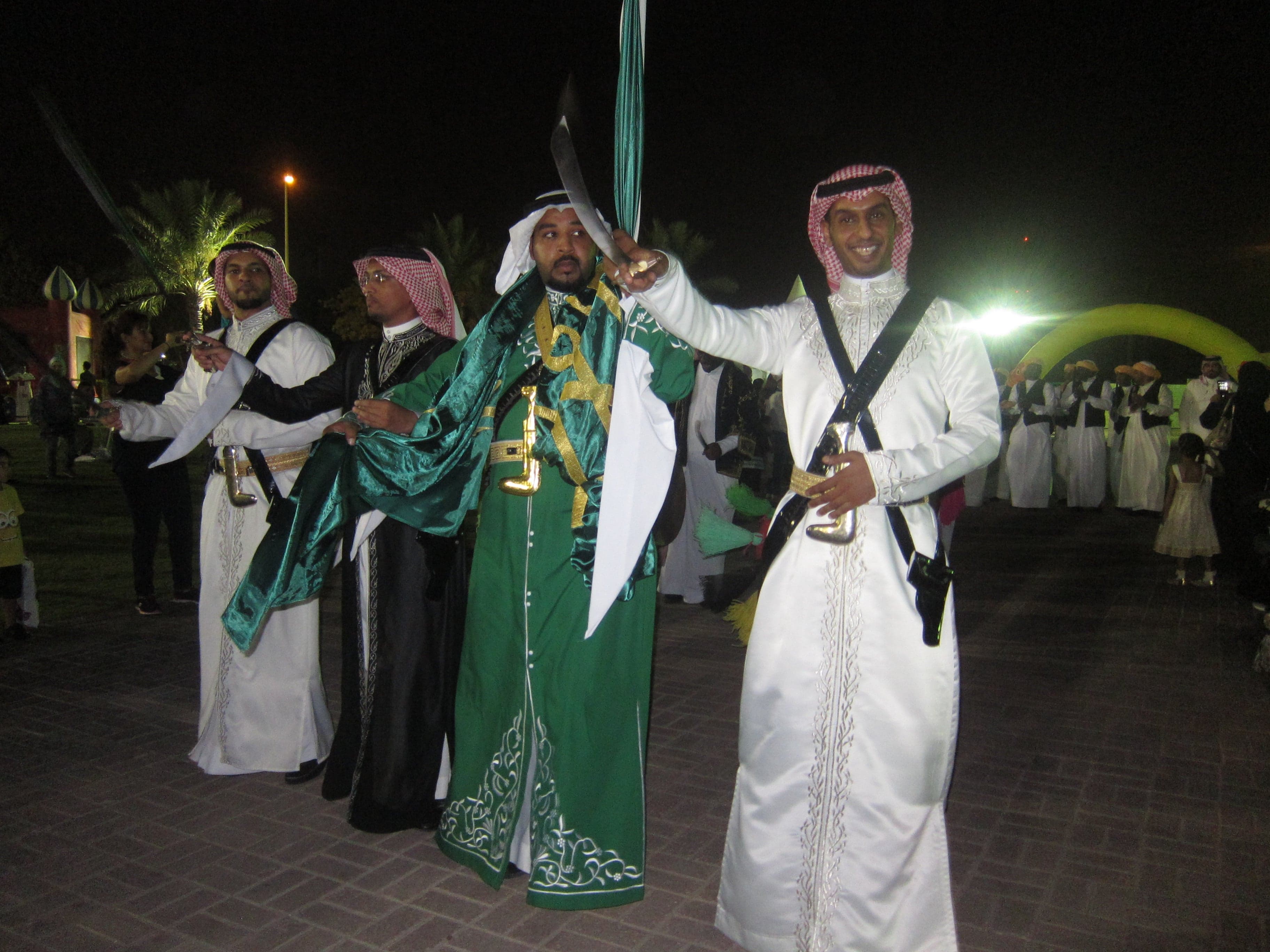 Men in white robes performing the Ardha sword dance in two long rows