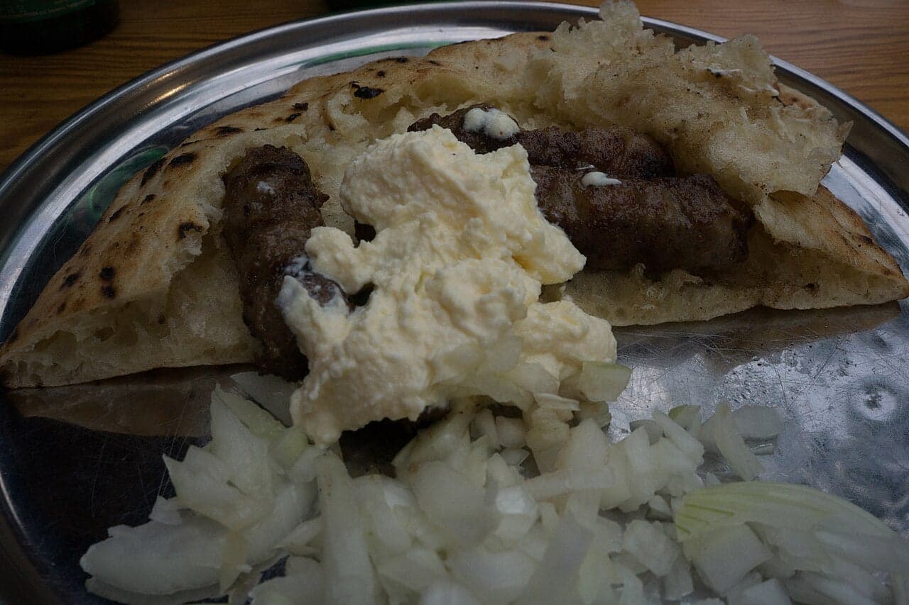 A plate of cevapi grilled meat rolls served with flatbread and chopped onion