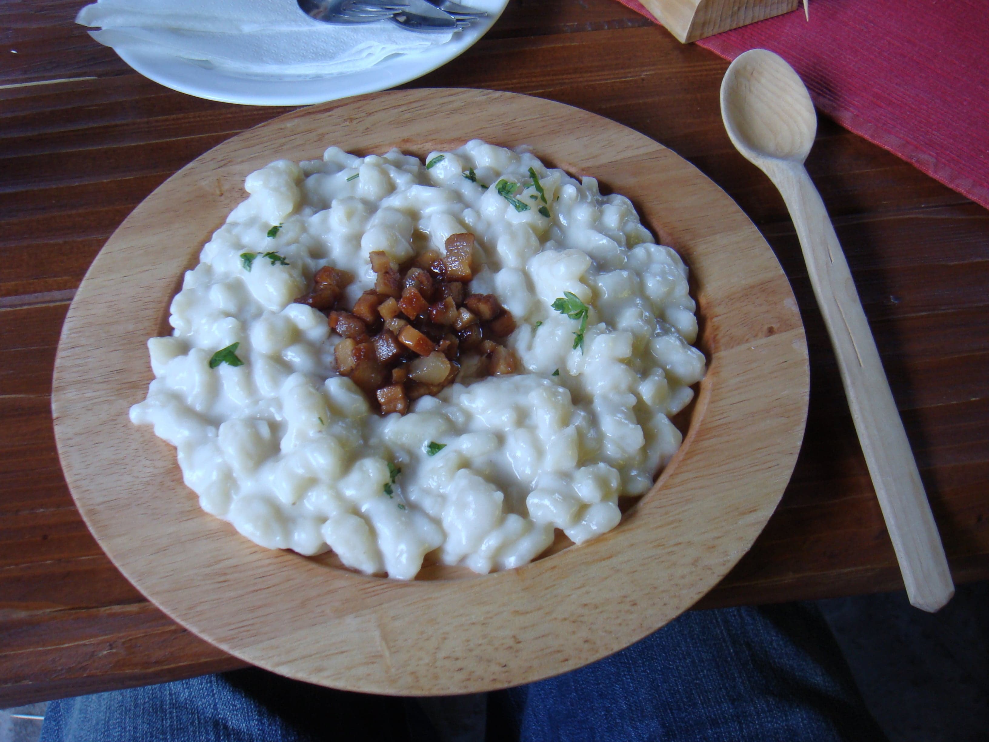 A bowl of small white potato dumplings topped with sheep cheese and crispy bacon pieces