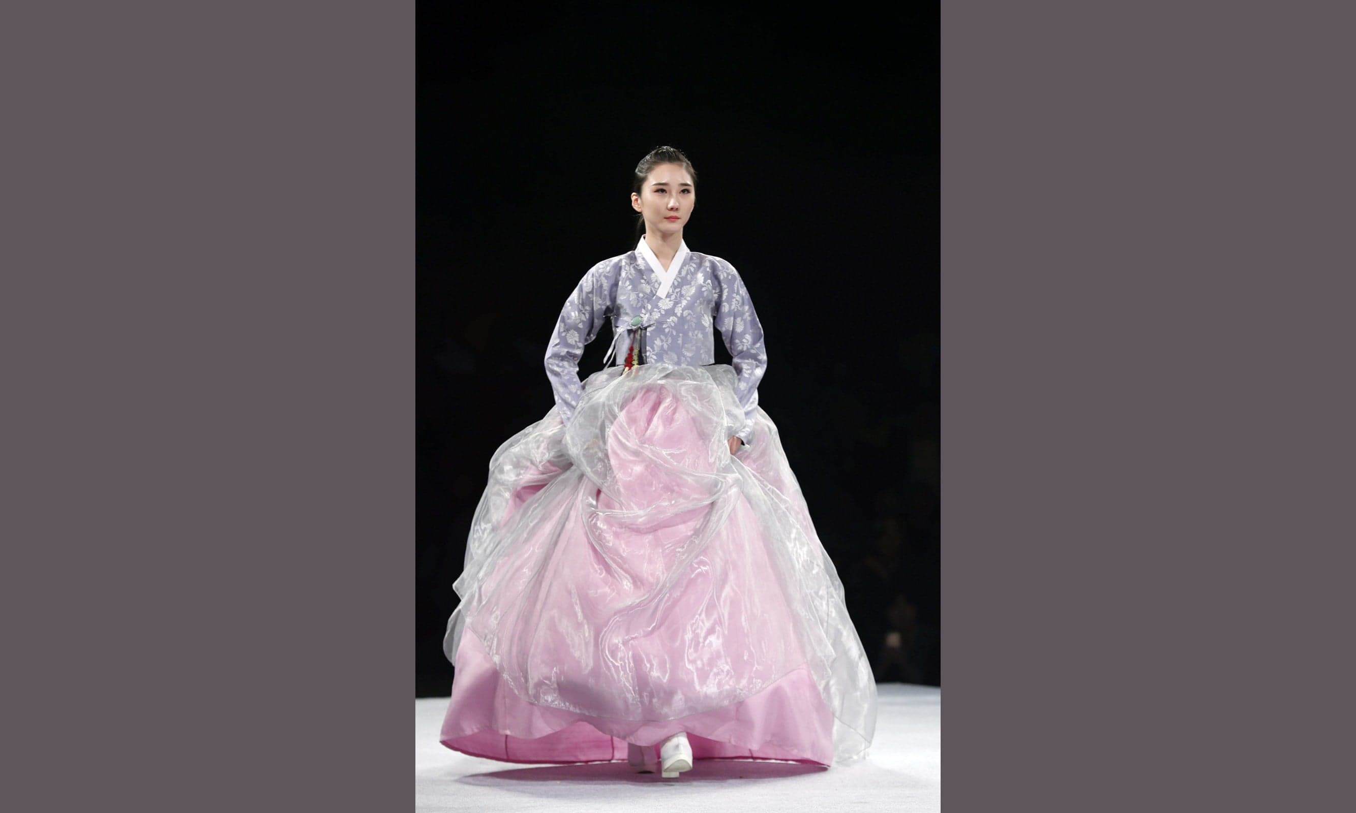 A model wearing a hanbok with a purple top and pink and silver skirt