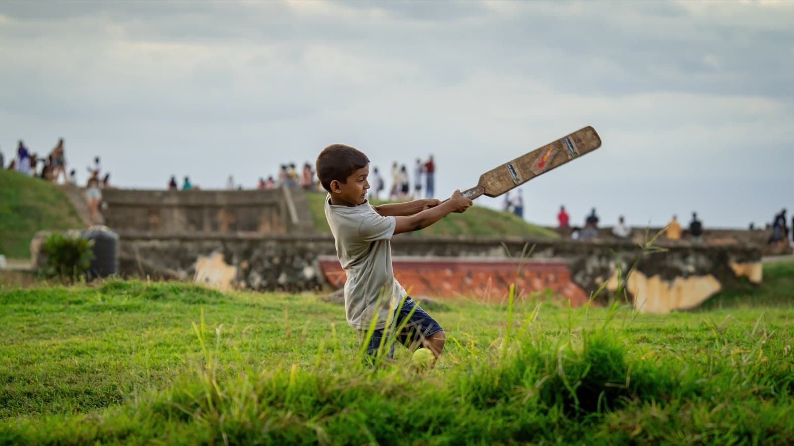 A boy swings a cricket bat on the green ramparts of Galle Fort, Sri Lanka
