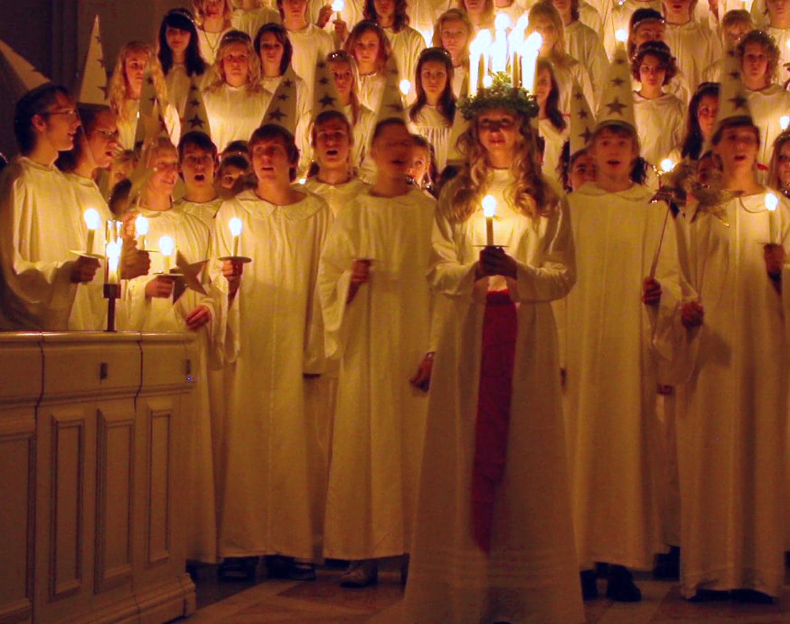 Swedish children in white robes singing in a Lucia procession, with one child wearing a crown of candles