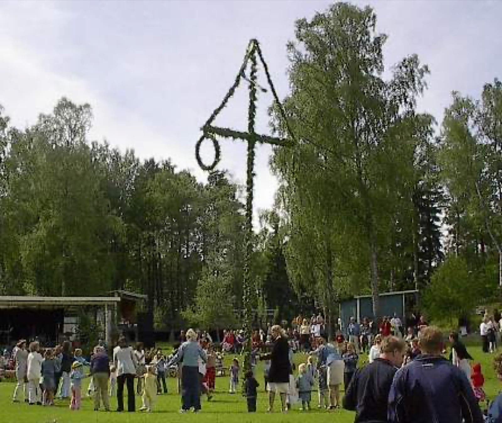 A Swedish midsummer maypole decorated with leaves and flowers, with people gathered around to dance