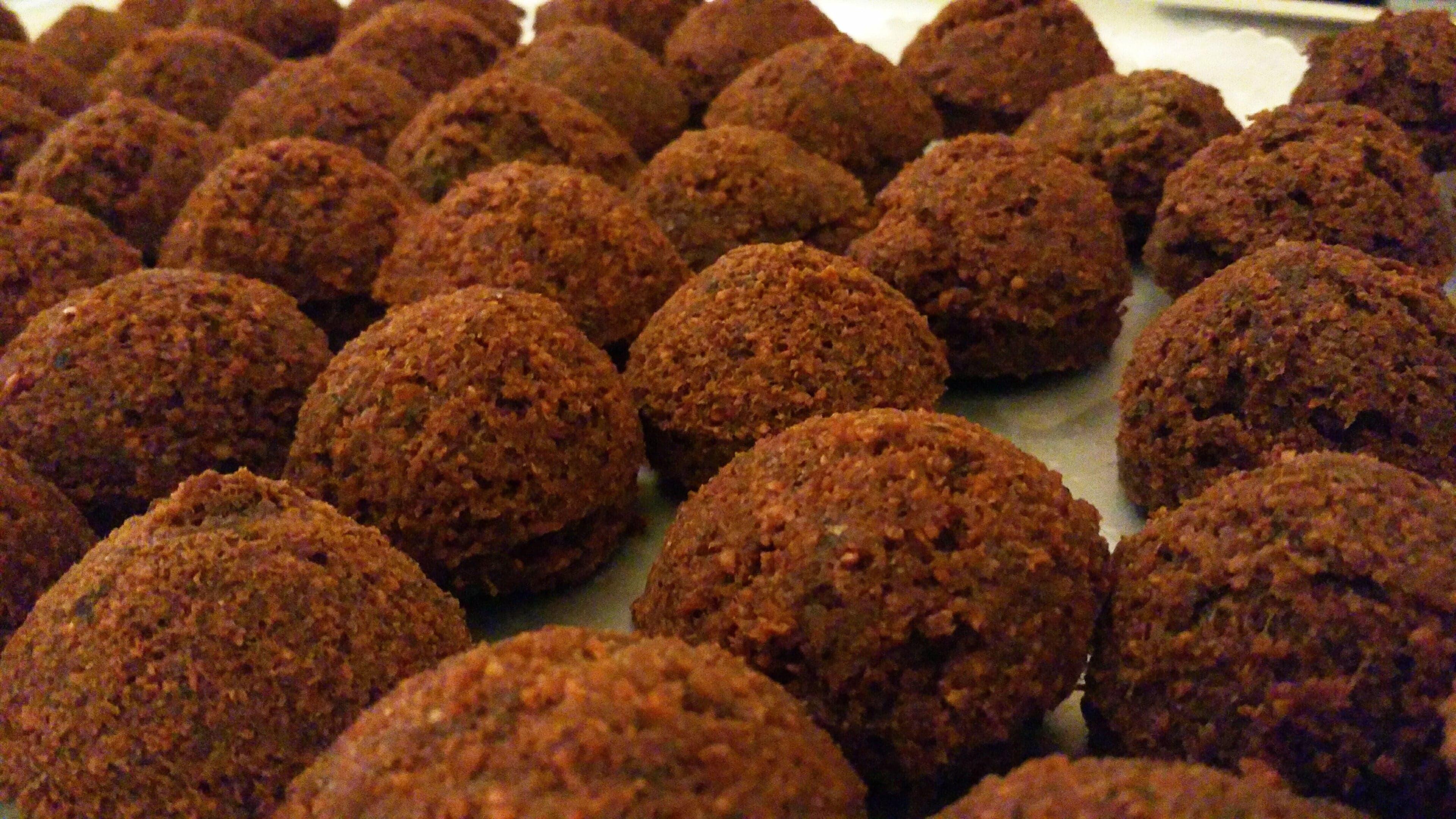 Golden-brown falafel balls piled on a plate with herbs and flatbread