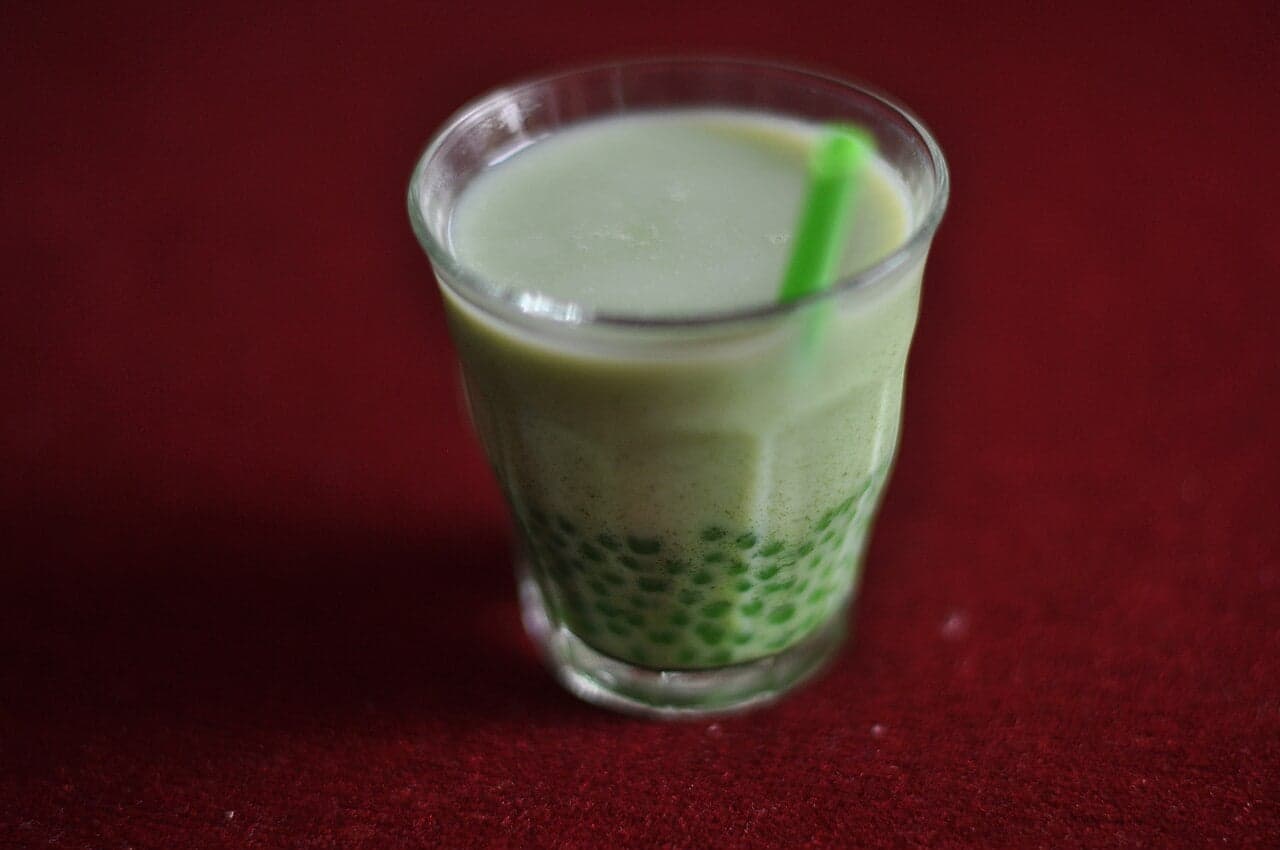 A clear plastic cup of bubble tea with dark tapioca pearls at the bottom and a fat straw