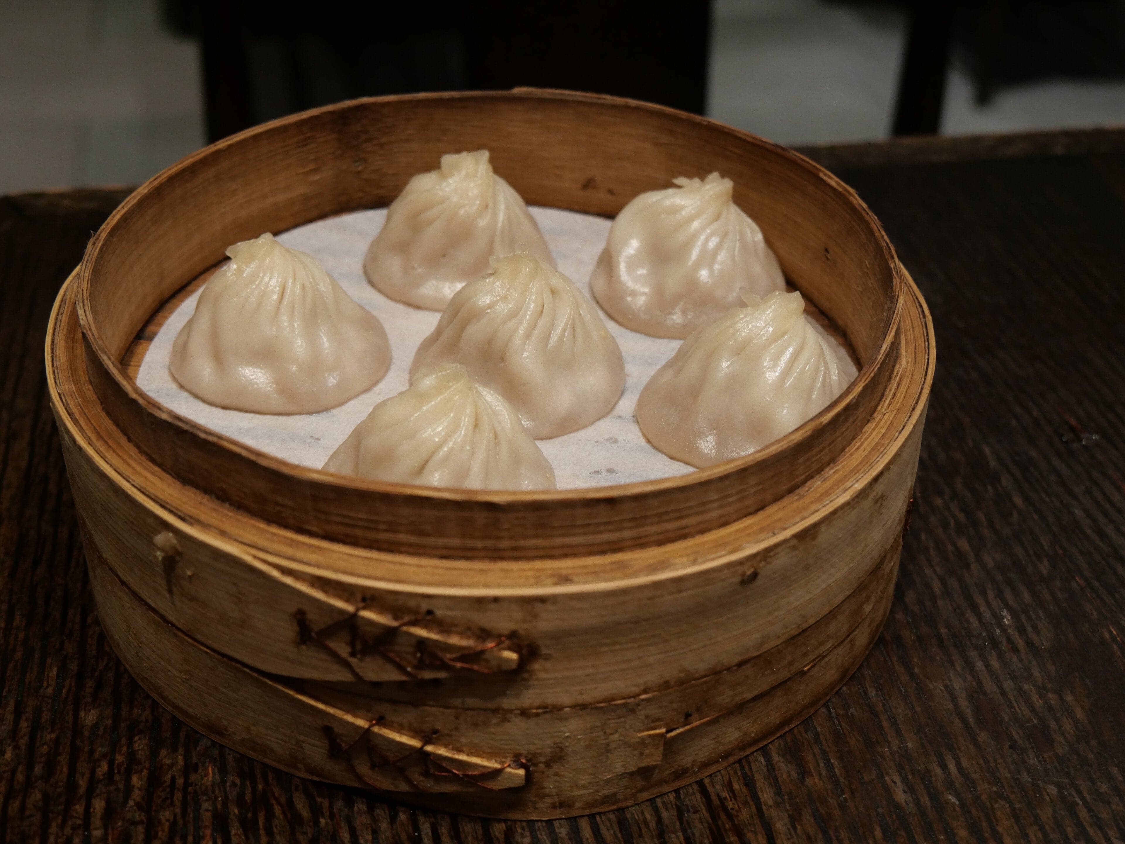 A bamboo steamer of xiao long bao soup dumplings with tiny pleats on top