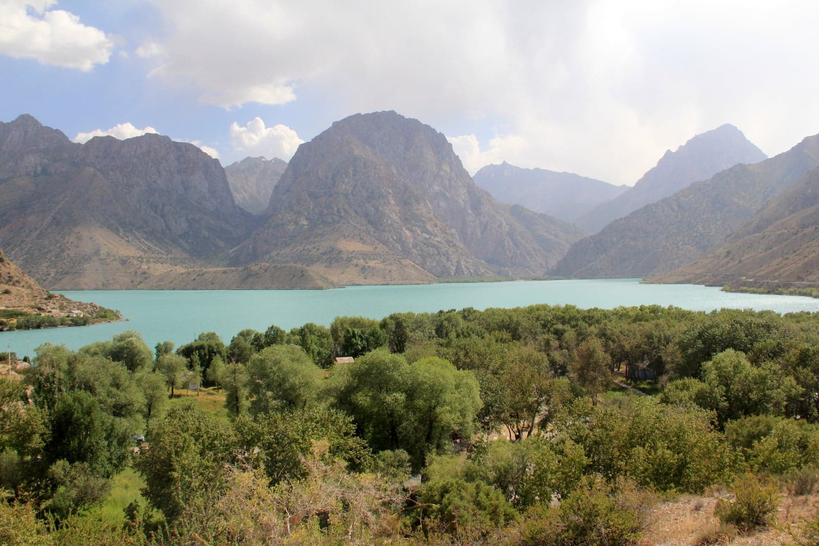 Brilliant turquoise water of Iskanderkul Lake surrounded by forested mountain slopes