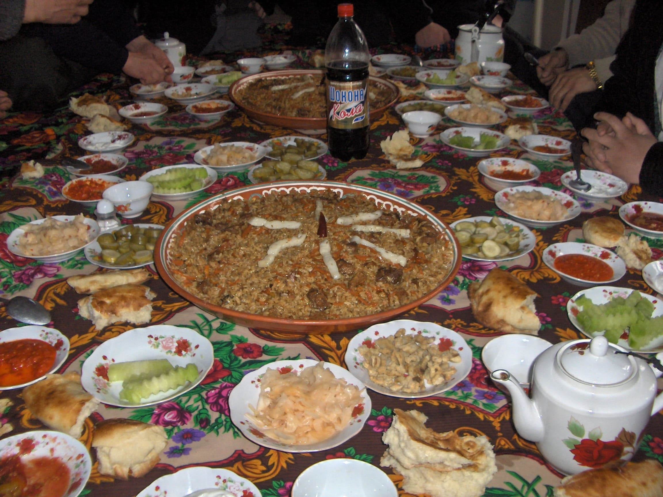A large mound of golden plov rice piled high in a wide cauldron with carrots and onions