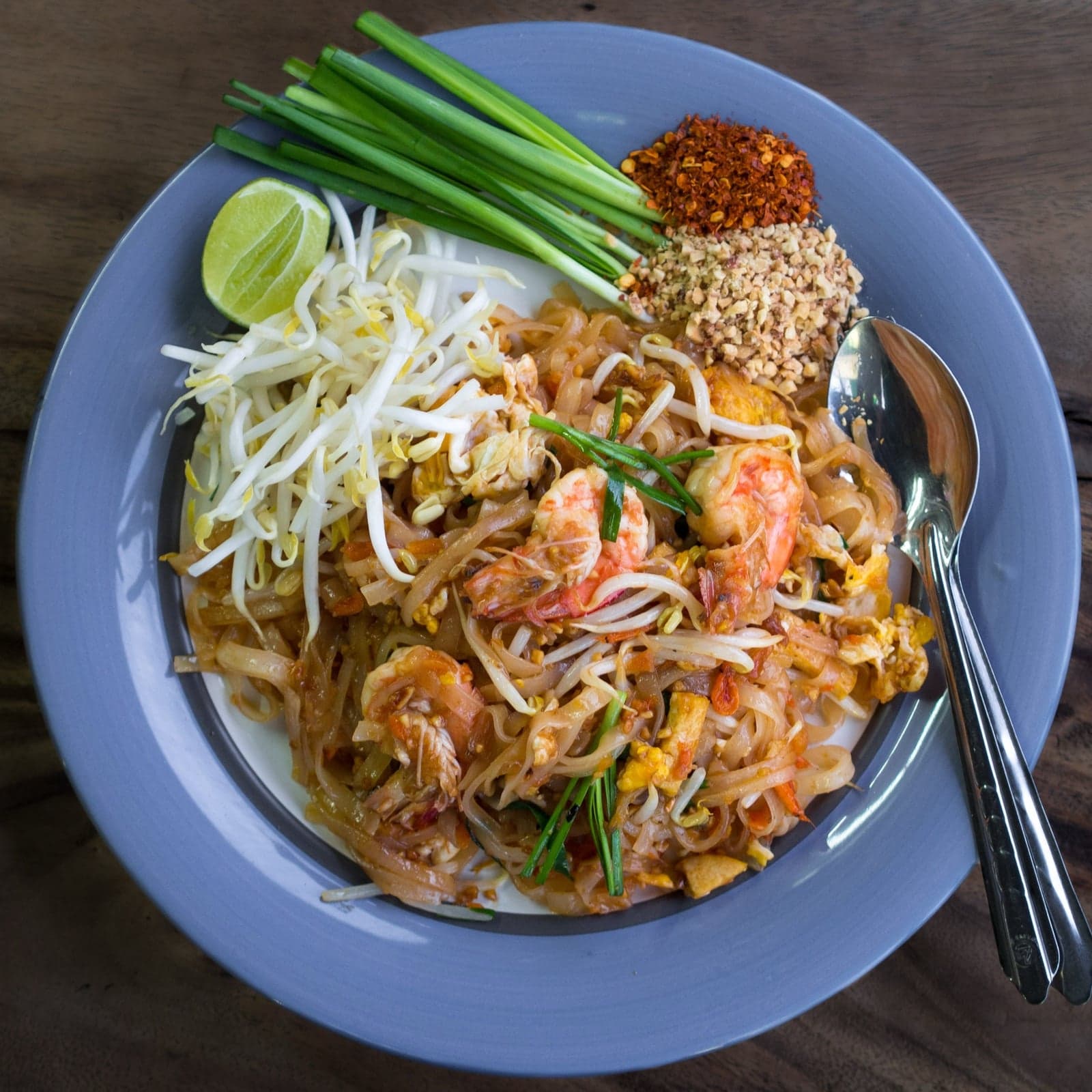 A bowl of pad thai with prawns, bean sprouts, lime and crushed peanuts