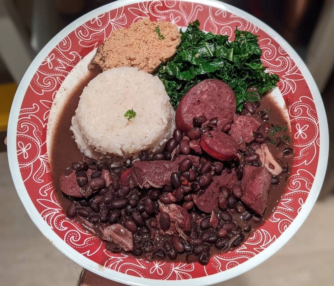 A pot of dark bean stew with herbs being ladled into a bowl